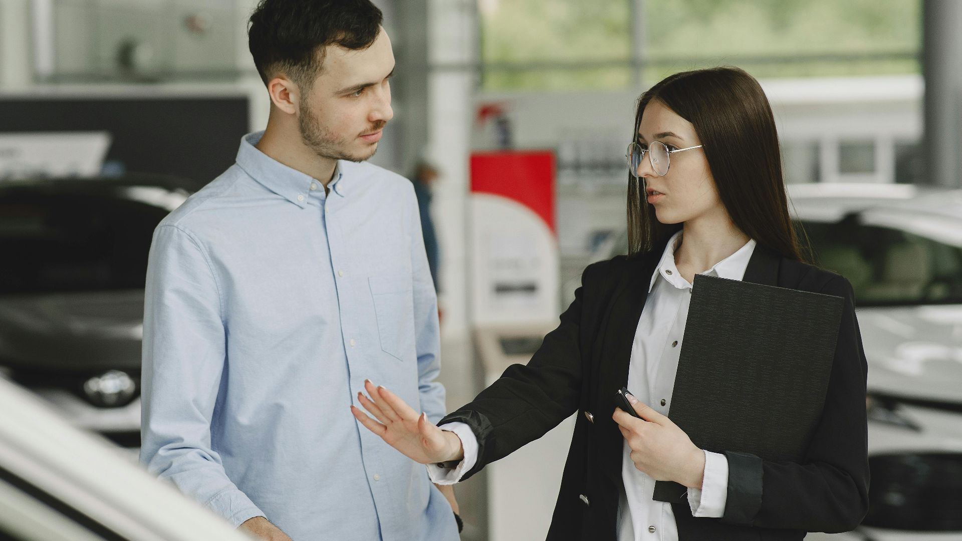 A salesperson and customer discussing car features in a dealership setting.