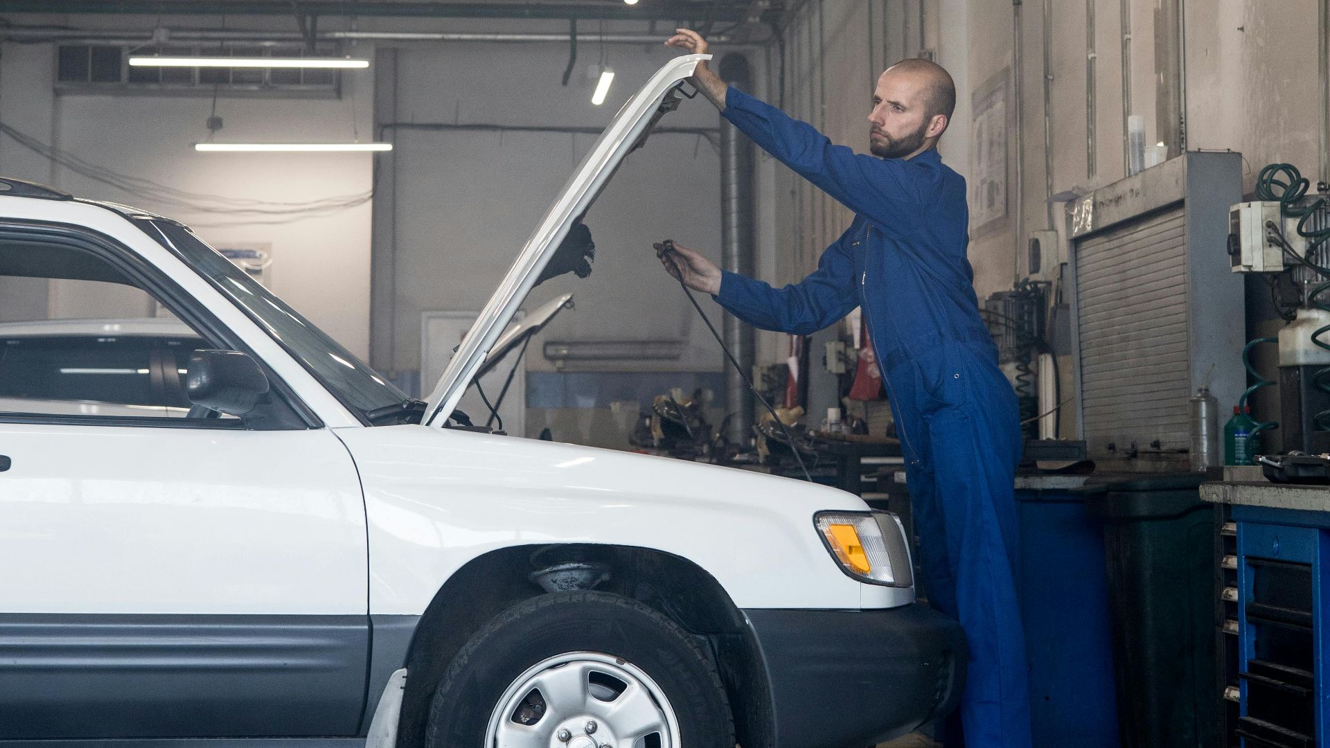 Mechanic checking under hood in auto repair shop for car maintenance.