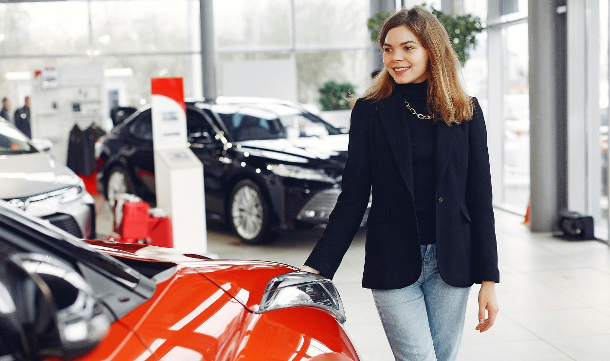 Smiling woman exploring cars in a bright showroom, expressing enthusiasm.