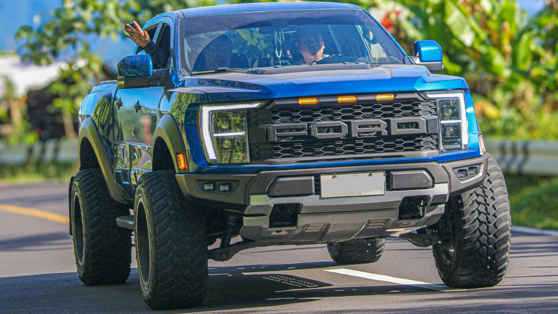 Off-road blue pick-up truck driving on a sunny scenic road with lush greenery.