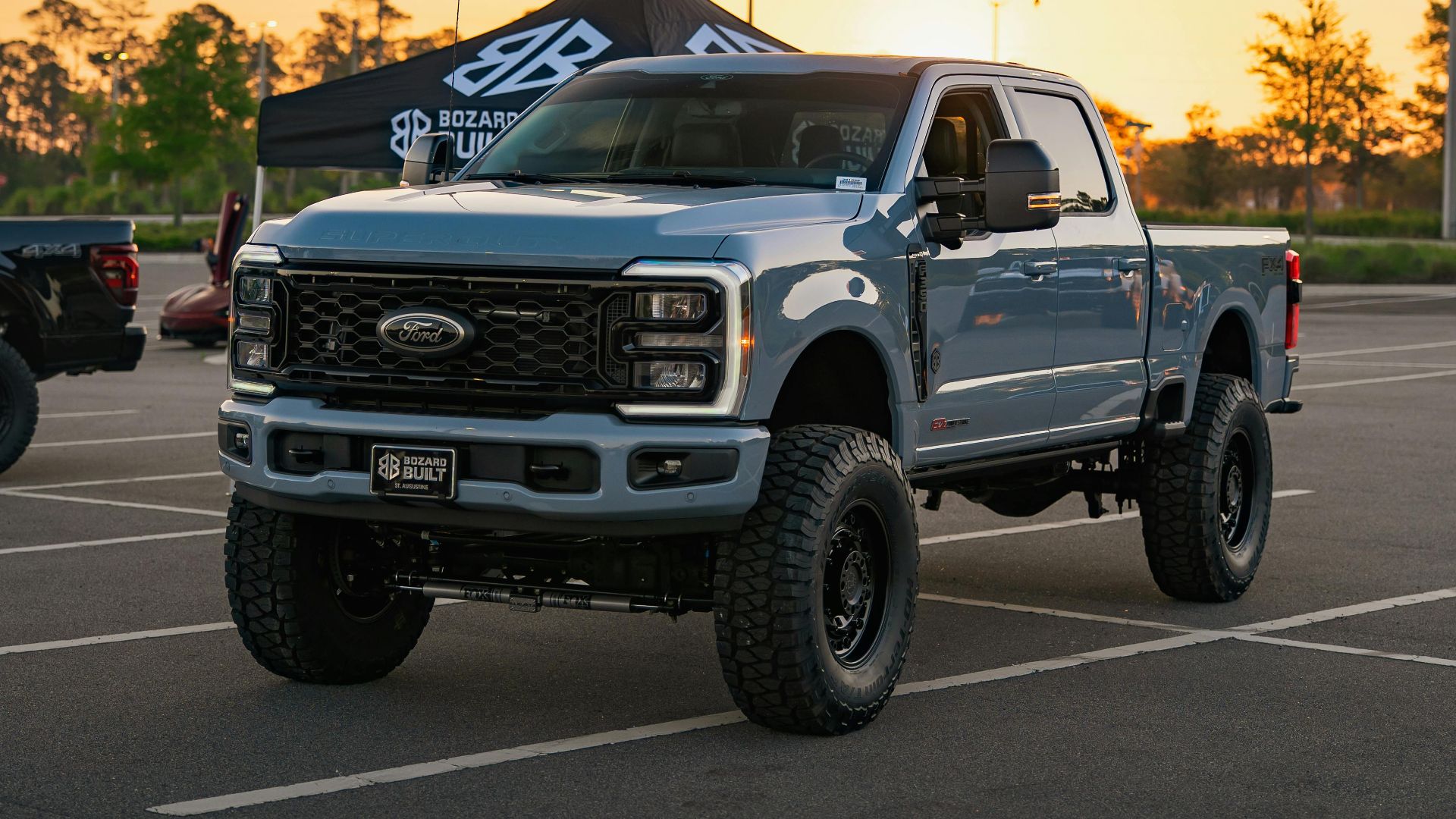 A blue pickup truck with lifted suspension parked outdoors during a vibrant sunset.