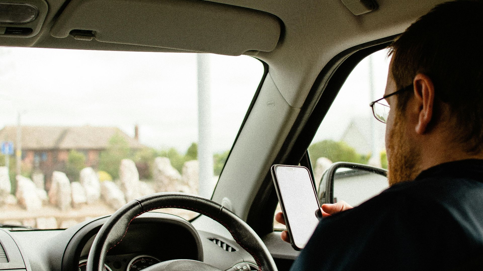 Back view of anonymous male in casual clothes sitting in car behind wheel and using smartphone
