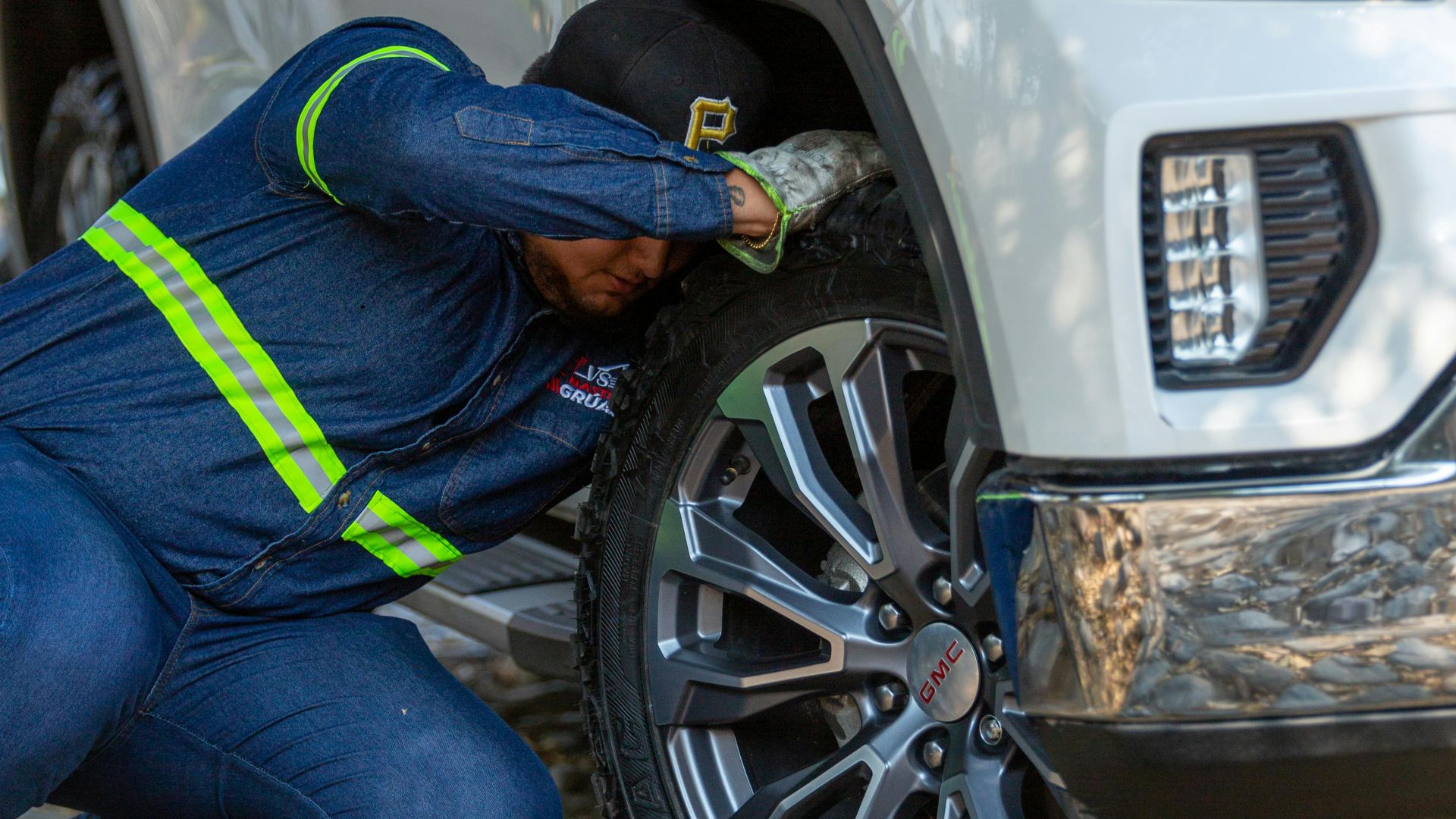 Mechanic working on the wheel of a white off-road vehicle outdoors, fixing a problem.