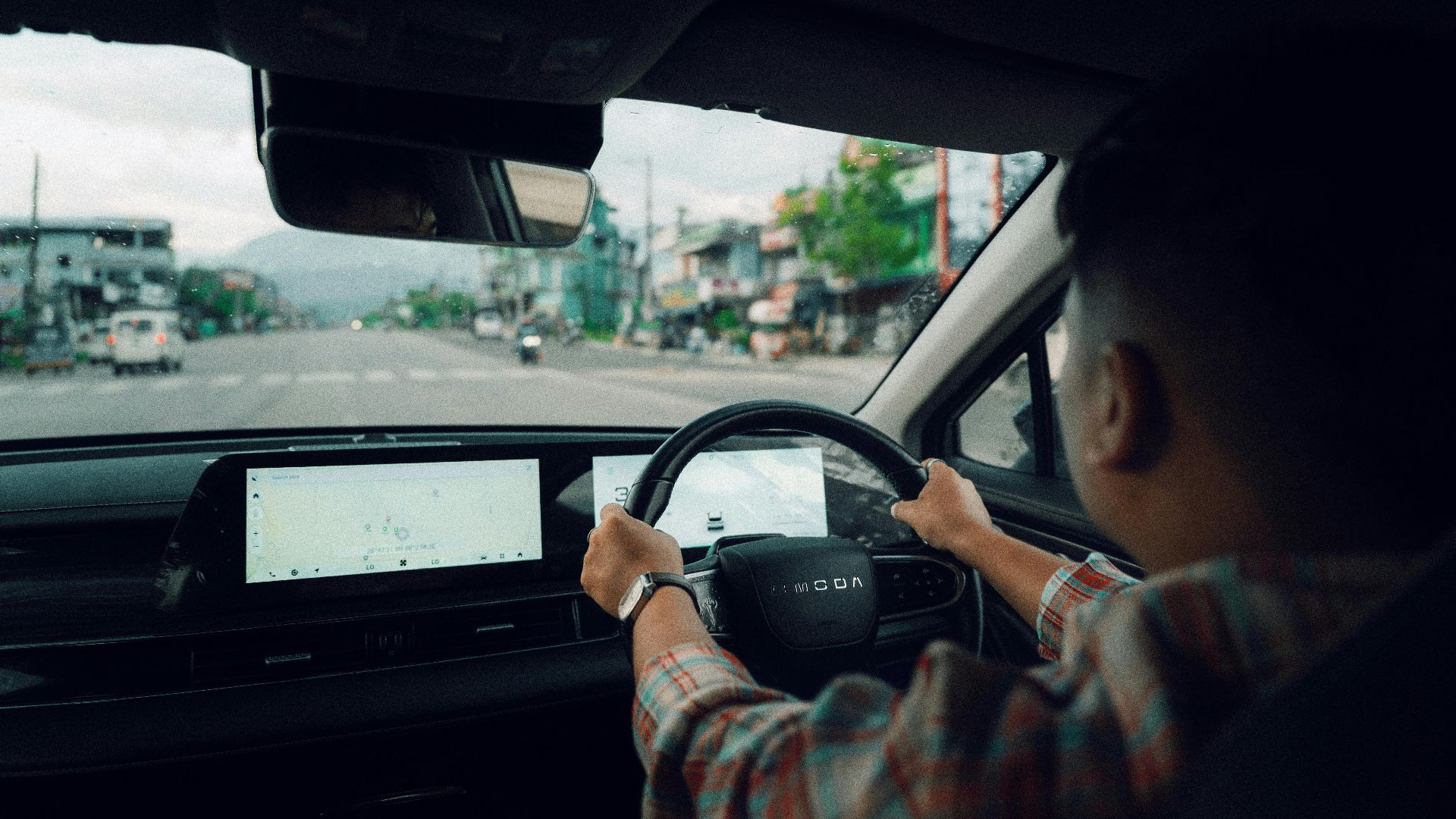Person driving a modern car through town, showing dashboard and road view.