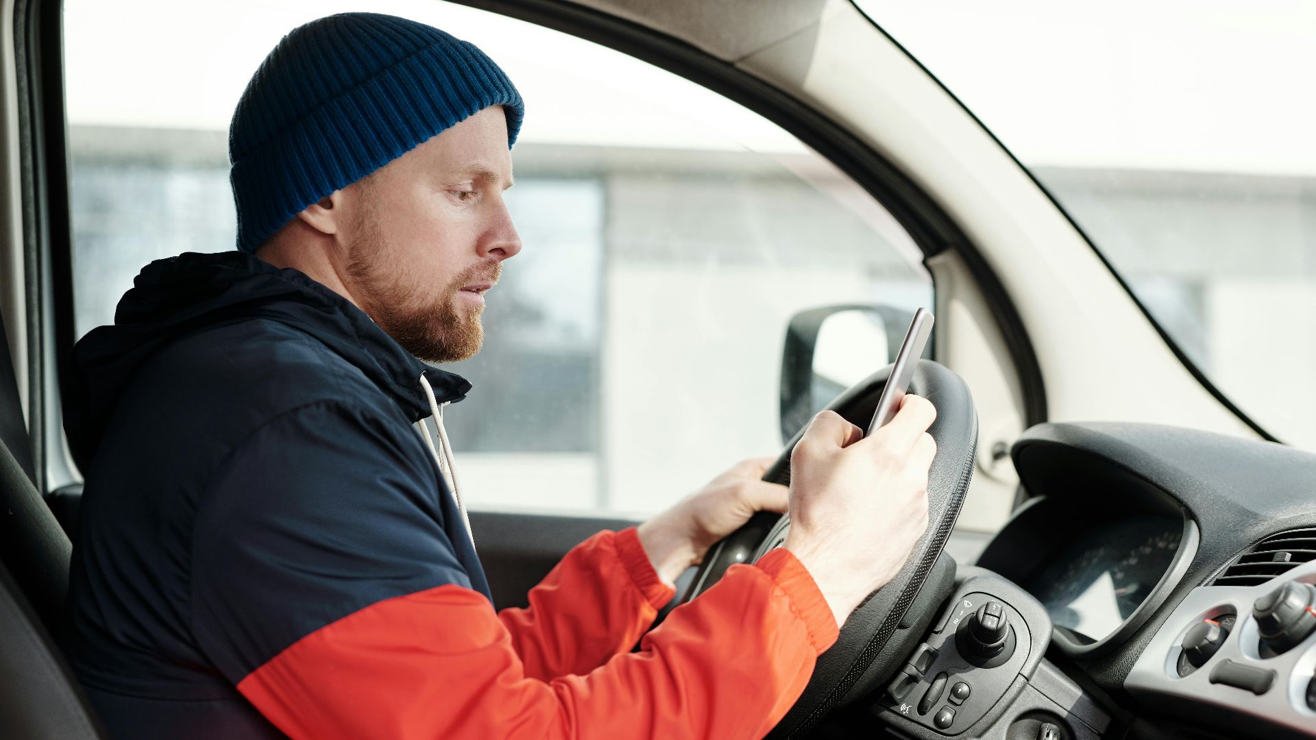 Distracted driver uses a smartphone in a car, highlighting road safety concerns.