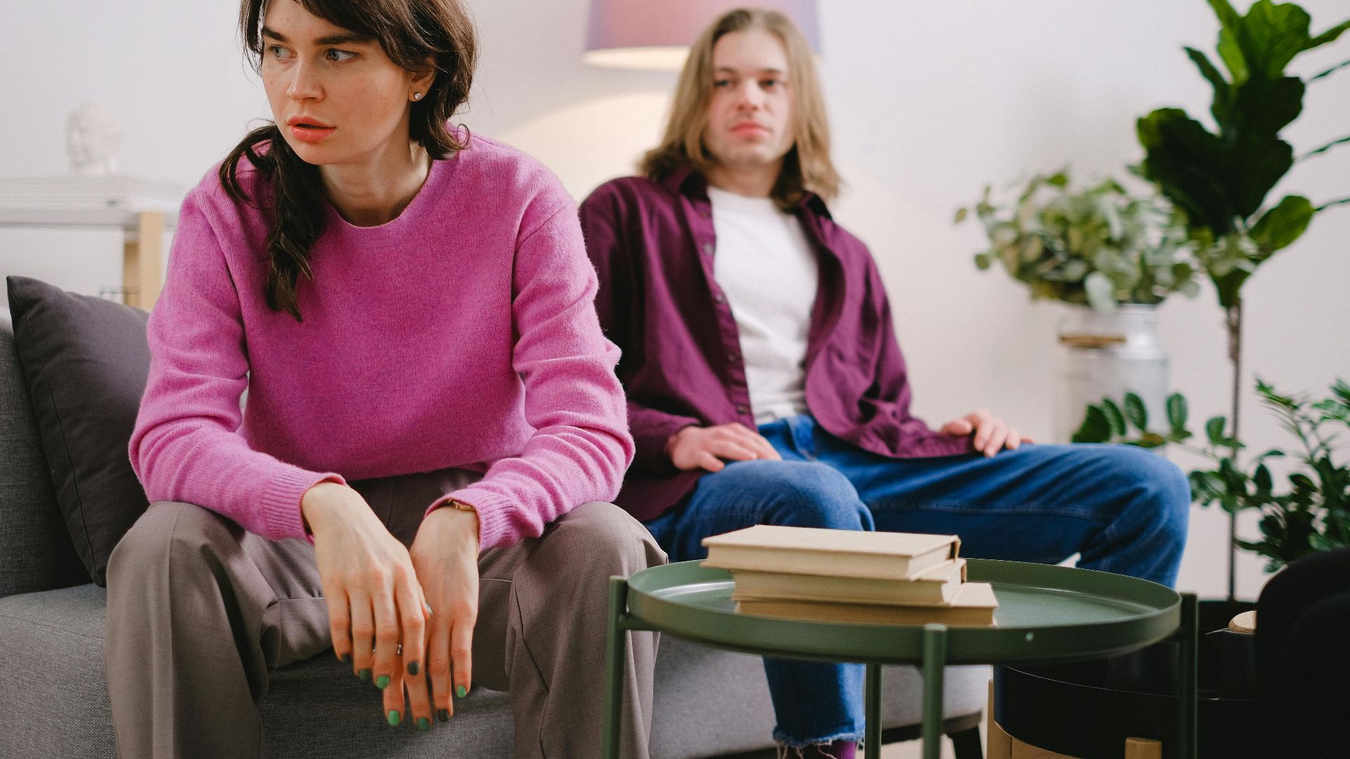A couple sitting on a sofa with thoughtful expressions, surrounded by home decor.