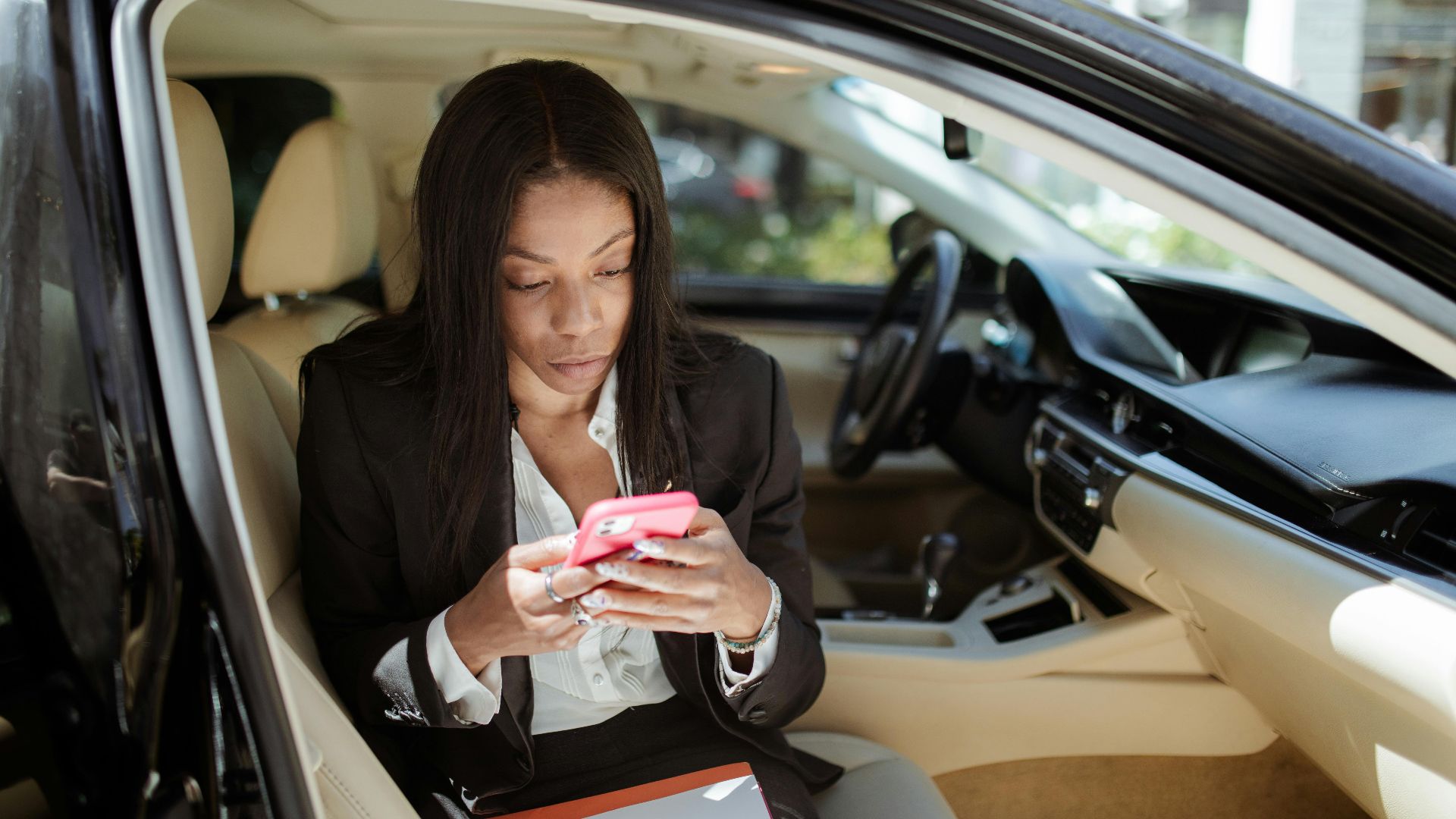 A businesswoman uses her smartphone while seated in a car, focusing intently on the screen.