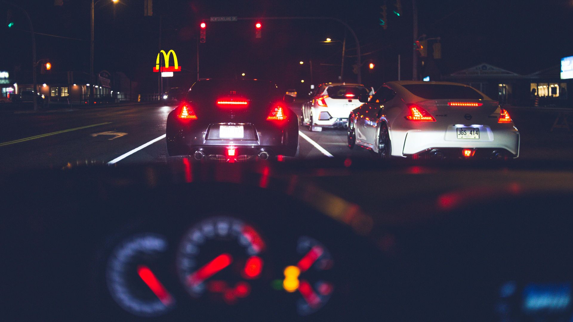 Stylish modern cars with glowing back lights driving on asphalt road in city at night