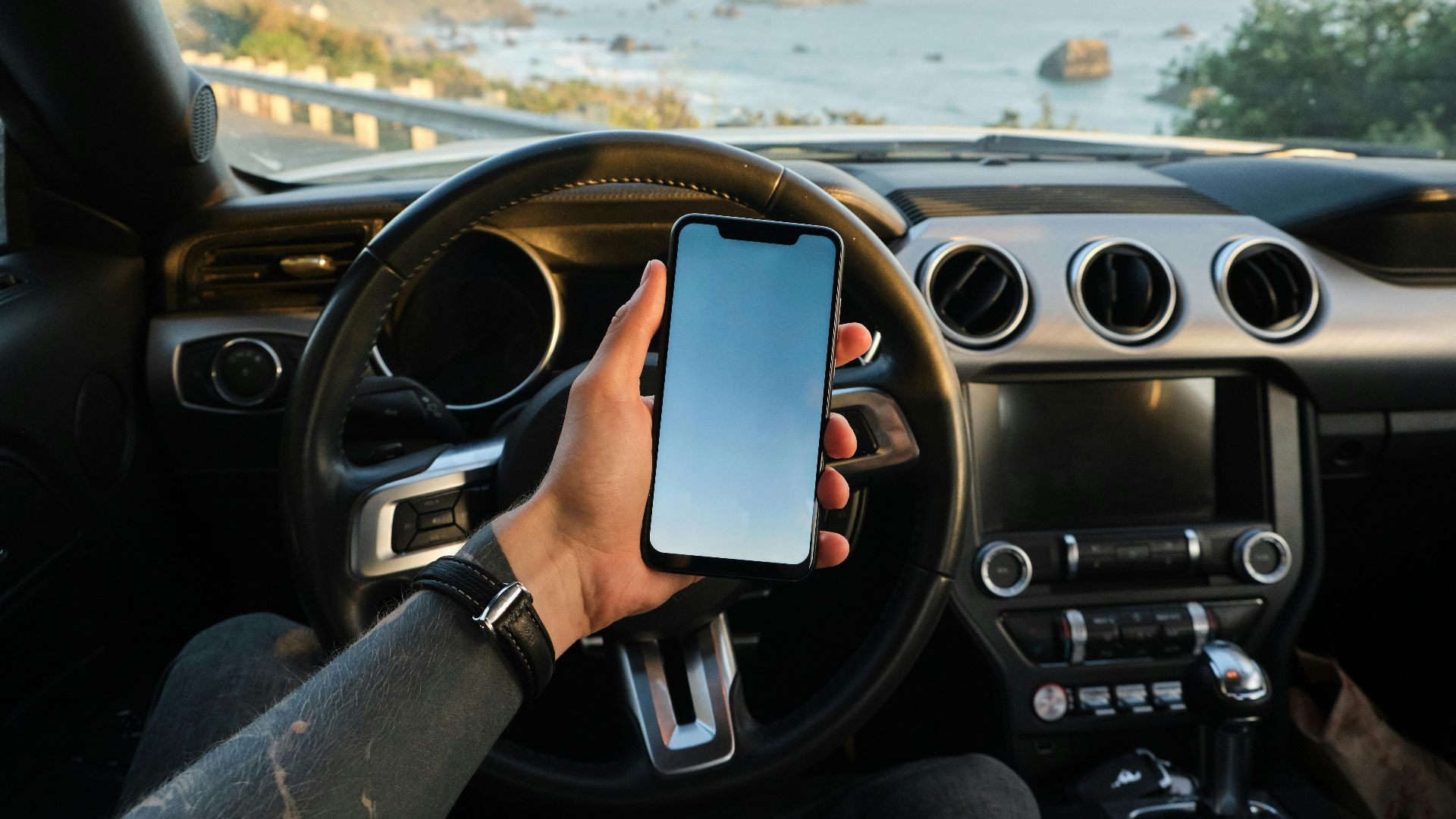 Crop anonymous guy with tattoo on hand navigating on mobile phone while driving car near sea