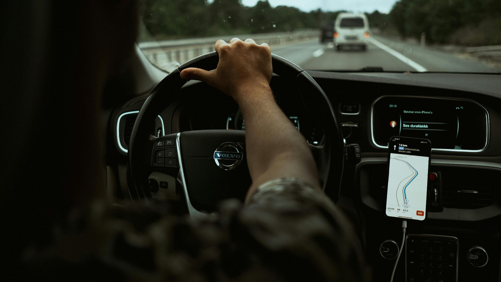 A driver navigates the highway with a smartphone GPS, showcasing modern car interior design.