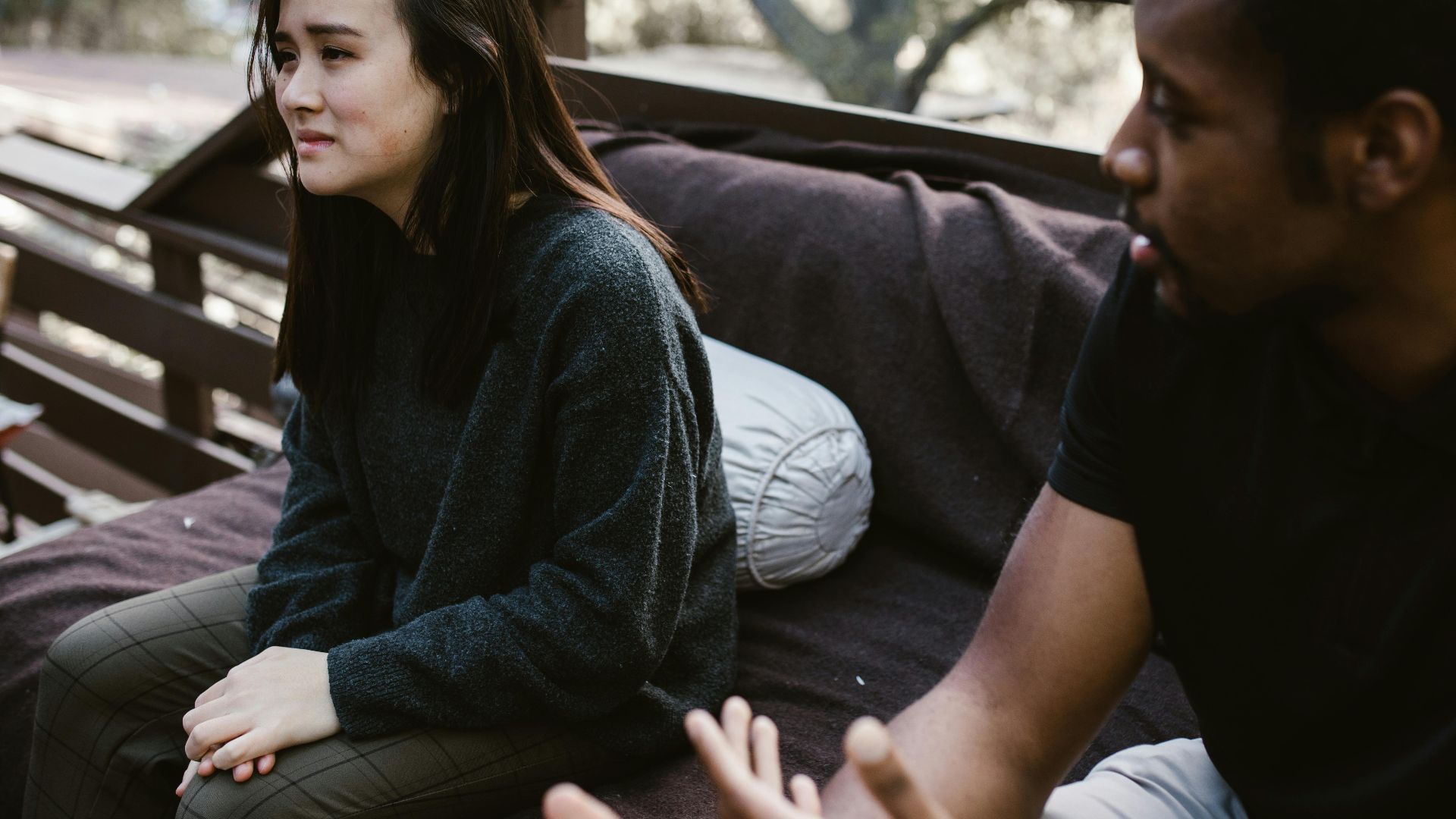 A man and woman having an emotional discussion on an outdoor bench.