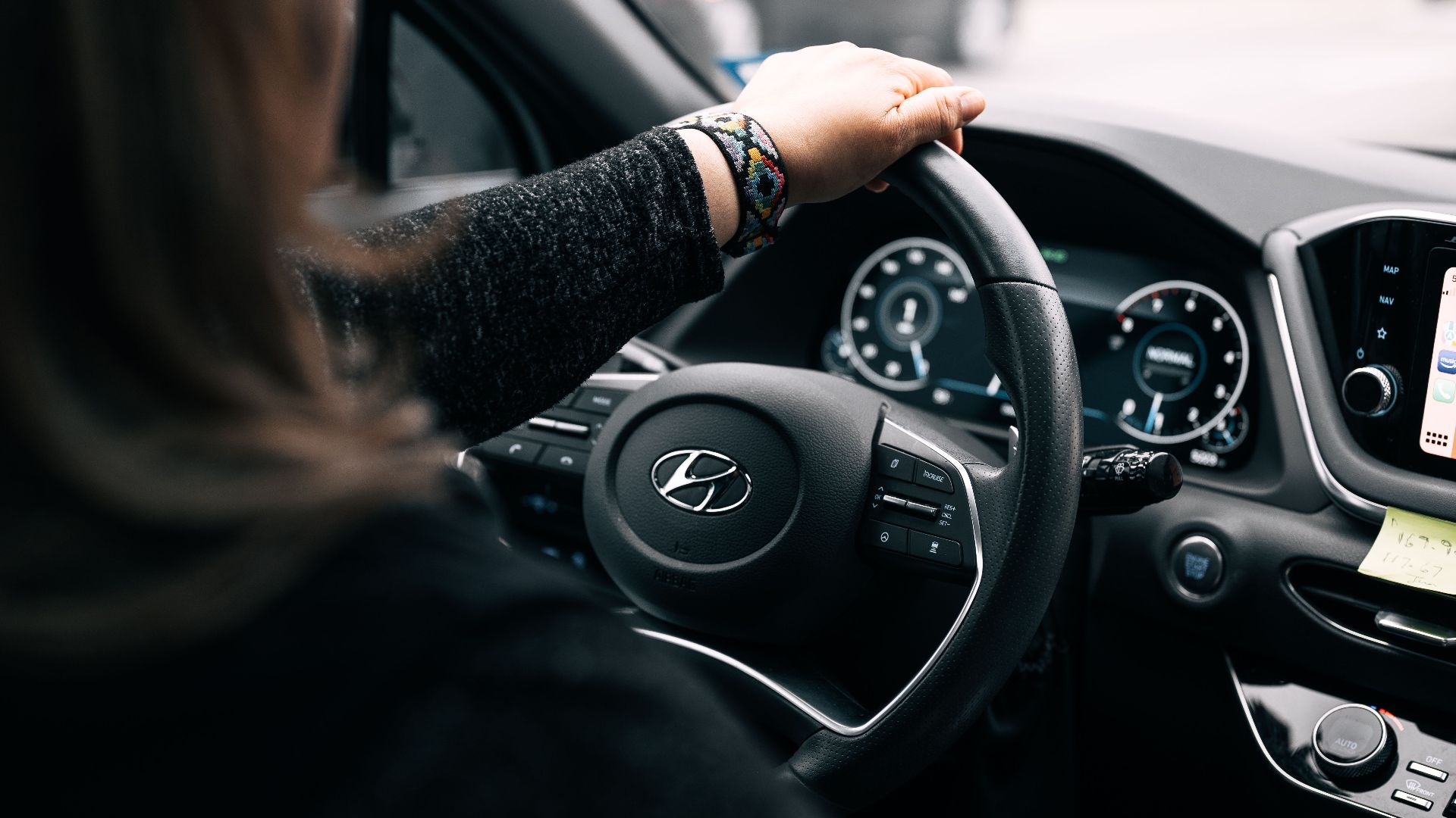 A woman driving a Hyundai car, focusing on the steering wheel and dashboard controls.