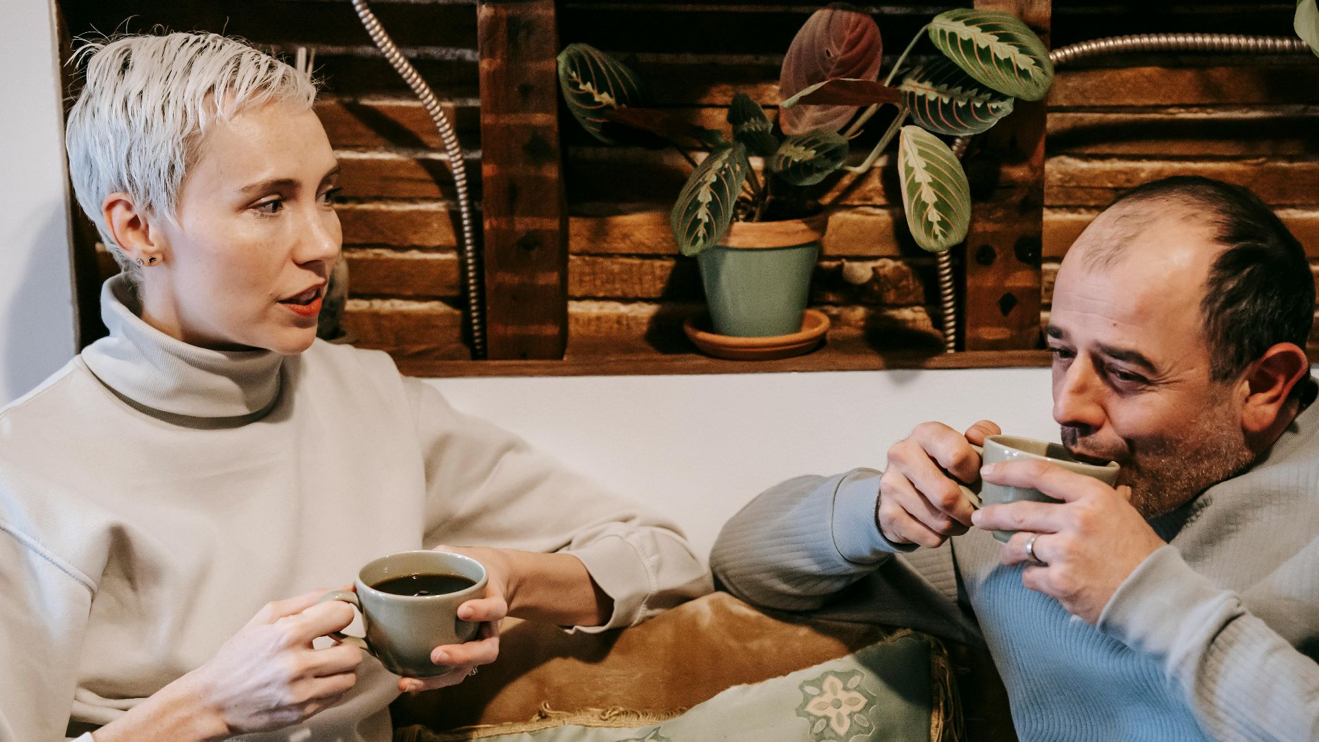 Calm multiracial friends in casual clothes drinking cups of coffee and communicating while spending time in cafe