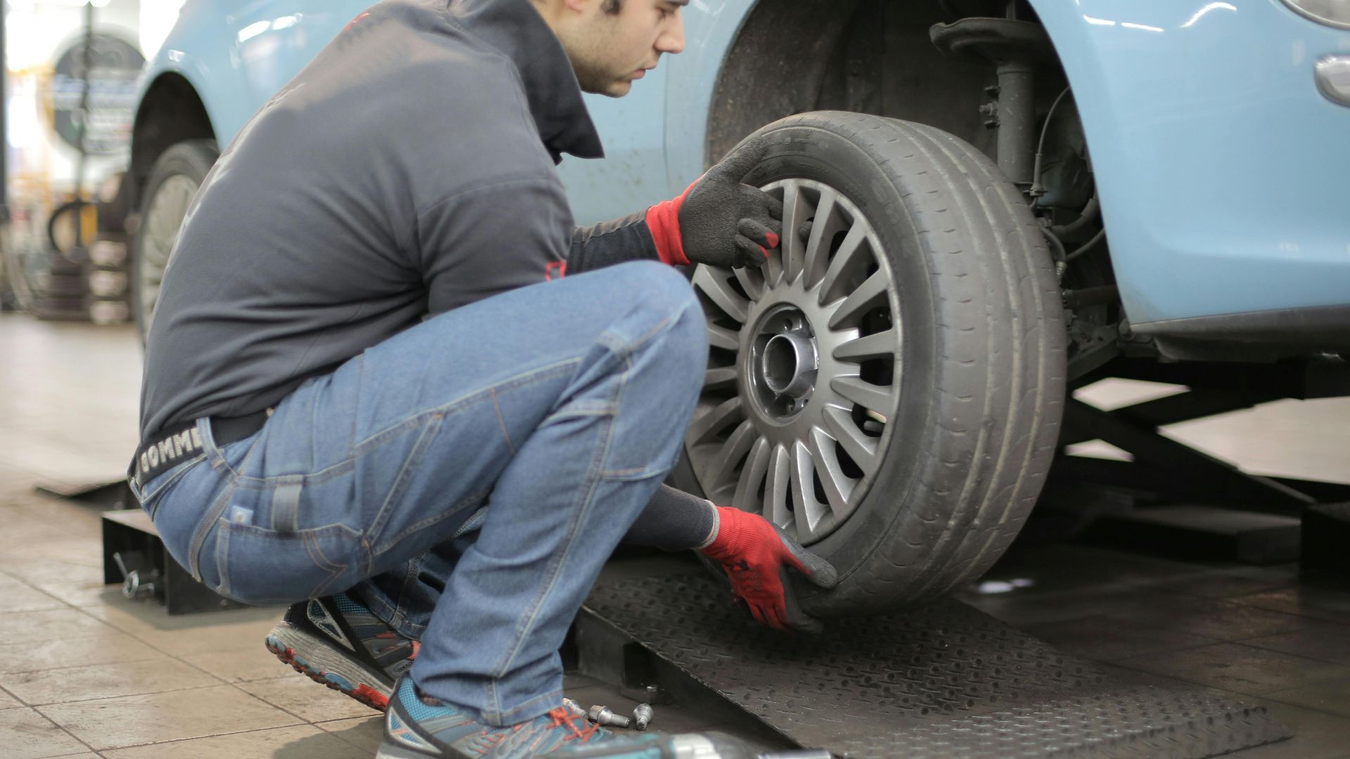 Mechanic changing a car tire indoors, using tools for vehicle maintenance.