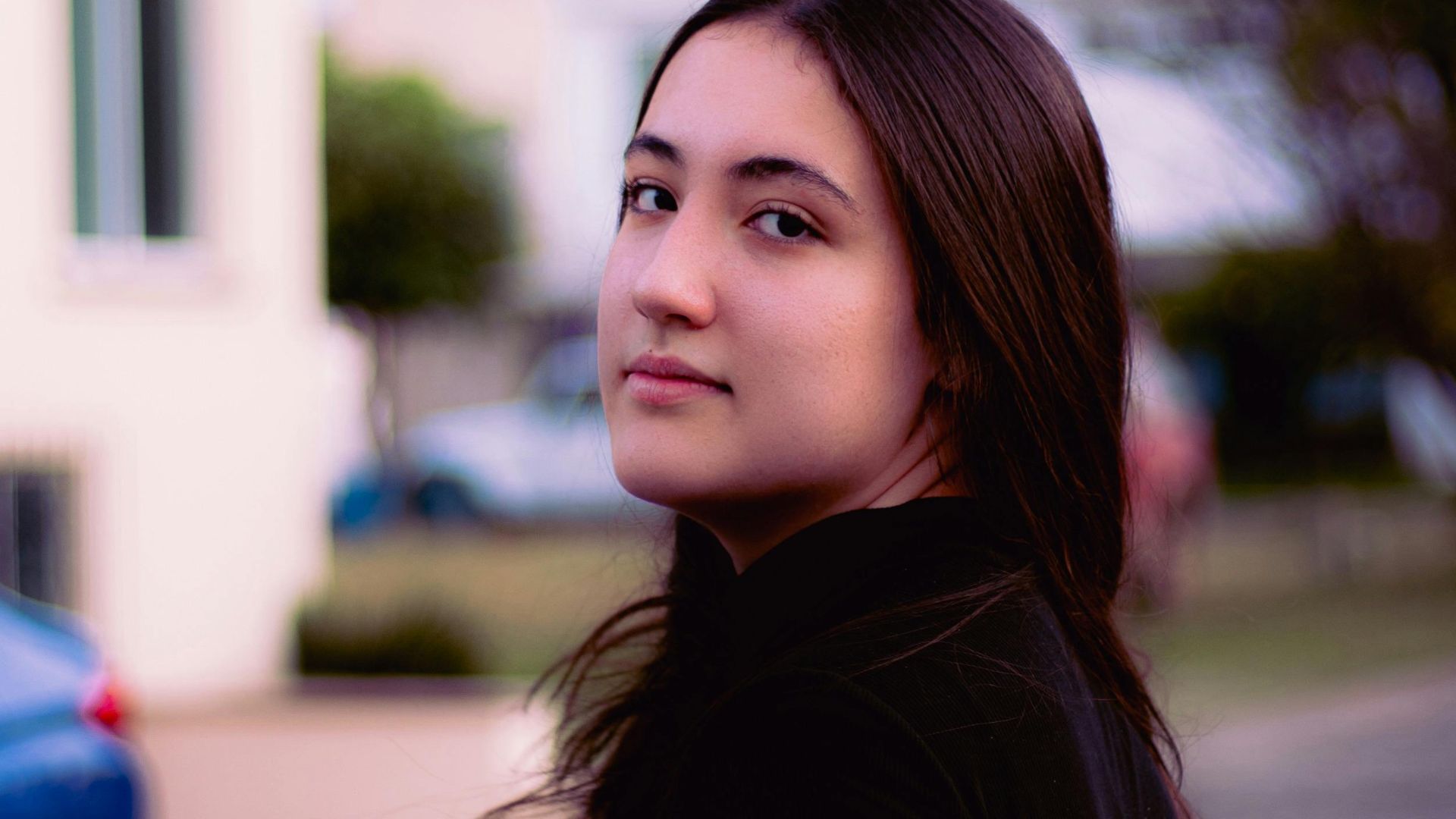 Portrait of a brunette woman looking over her shoulder on a city street during the day.