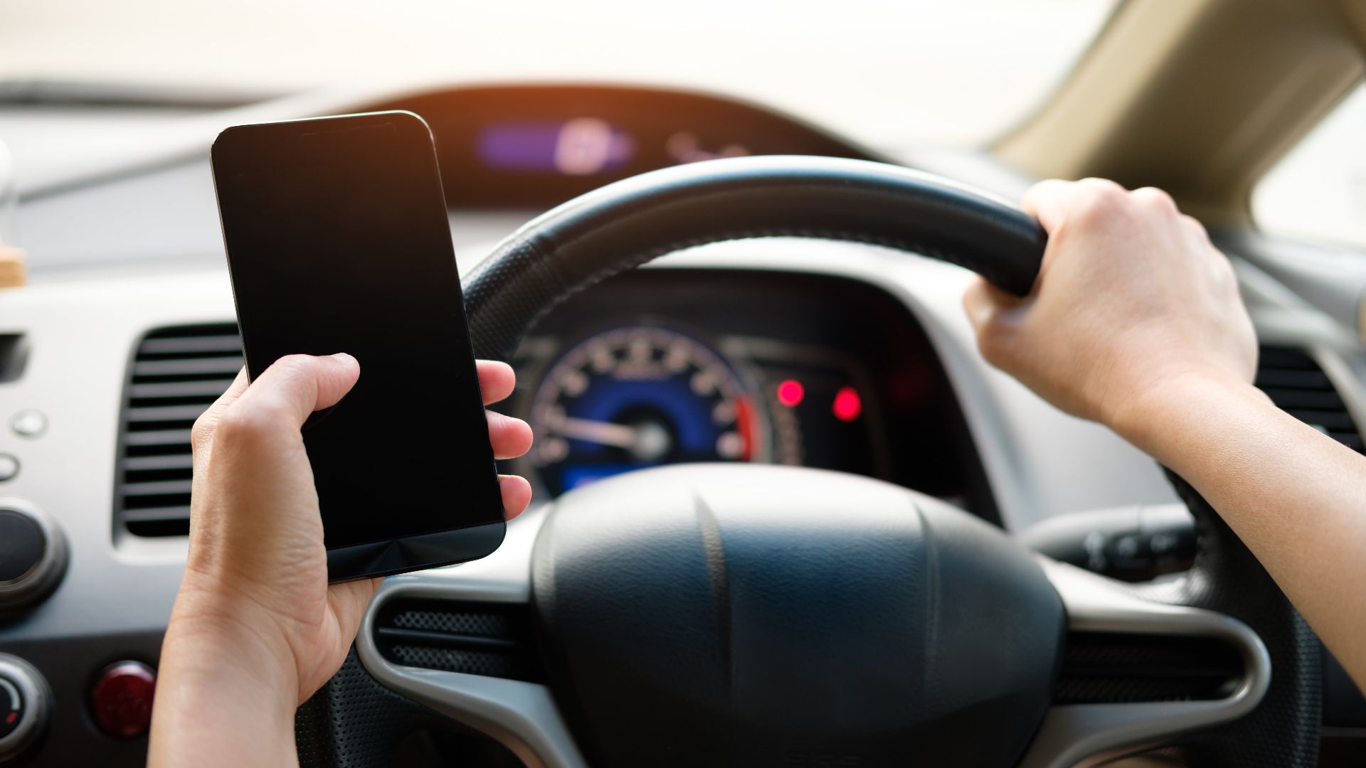 A driver uses a smartphone while steering a vehicle, showcasing distracted driving risks.
