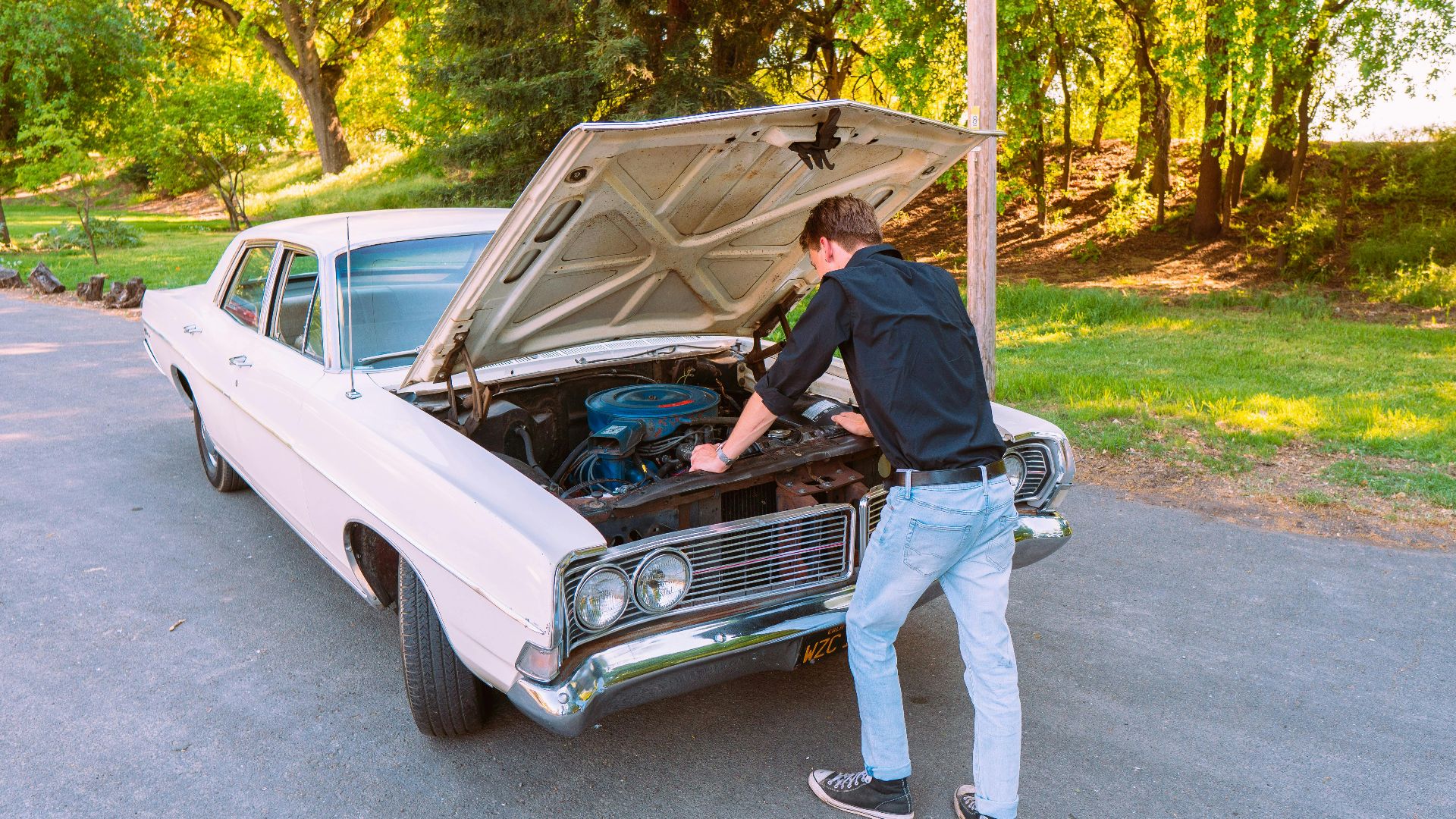 A man fixing a vintage car engine outdoors in Clarksburg, California, on a sunny day.
