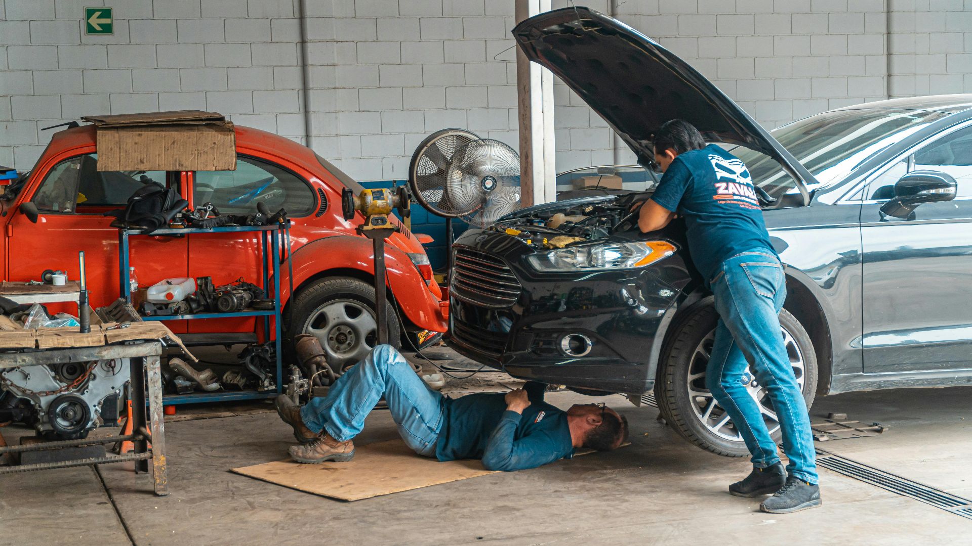 Mechanics working in an automotive workshop, repairing cars and performing maintenance.