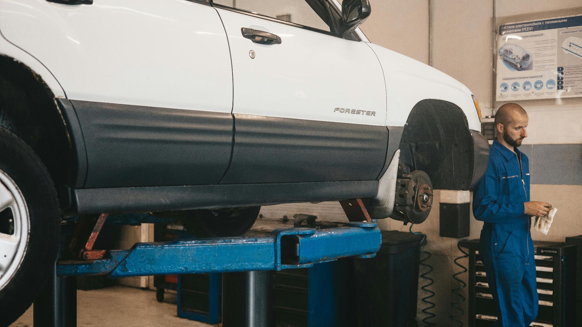 Mechanic evaluating a car on a lift for maintenance in an auto workshop.