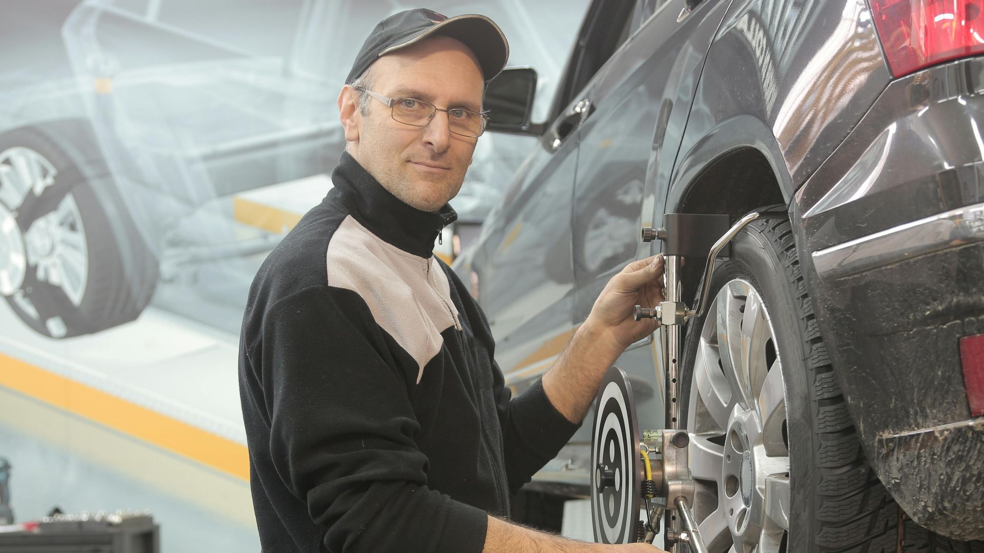 Mechanic performing wheel alignment on a car in a professional garage setting.