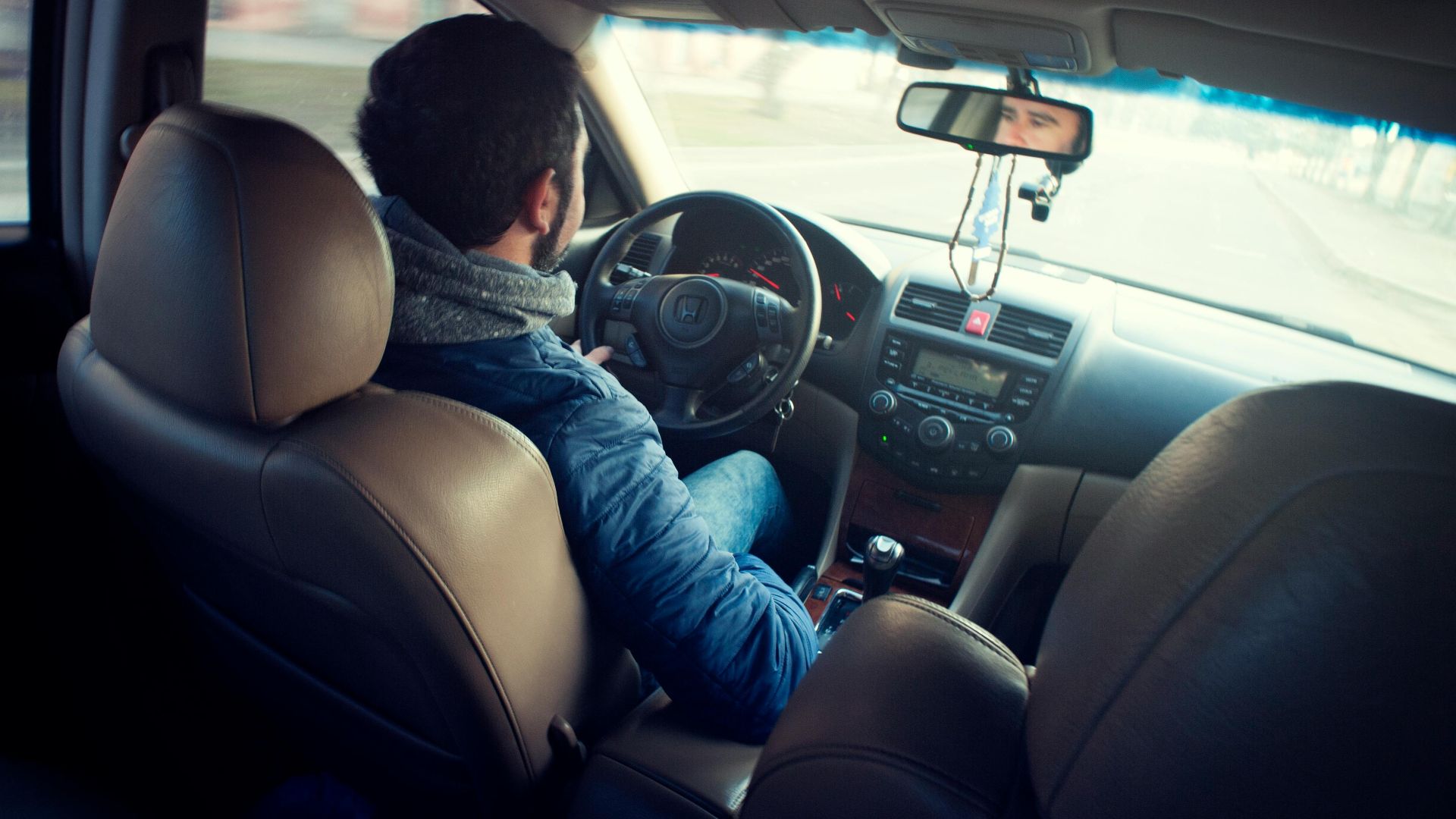 A man driving a car with focus on interior, dashboard, and steering wheel, captured from the backseat.