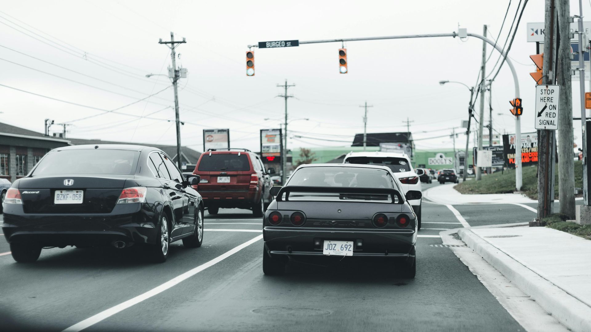 A busy road traffic scene with multiple cars and stop lights under cloudy skies.