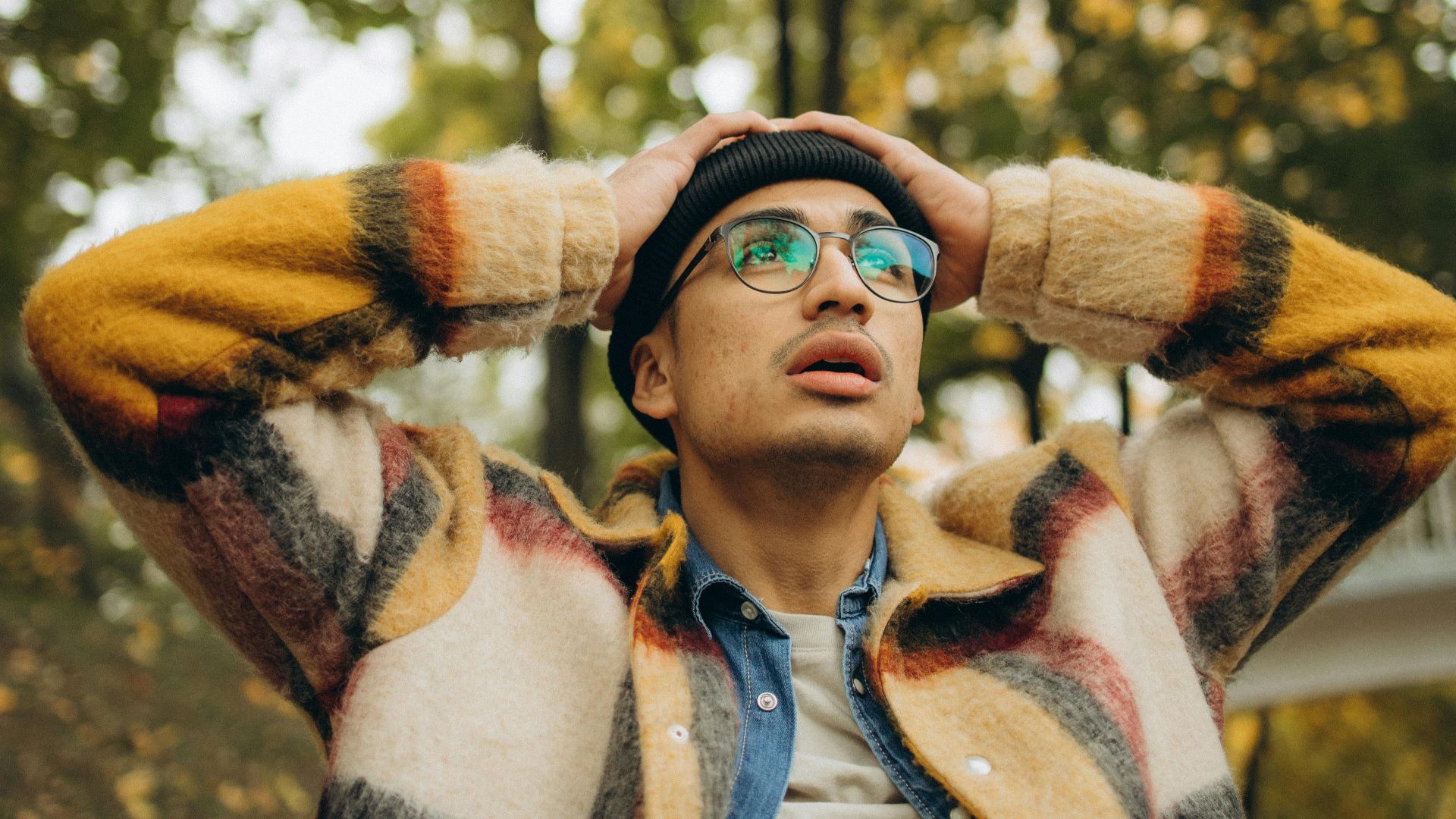 A young man wearing glasses looks surprised in an autumn setting. Perfect for lifestyle themes.