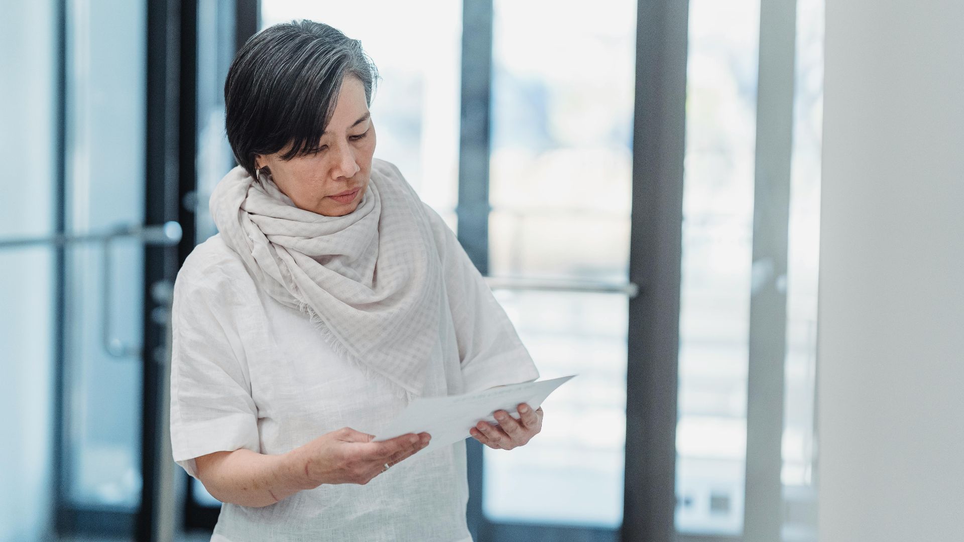 A senior woman reading papers in a bright office setting, exhibiting focus and concentration.