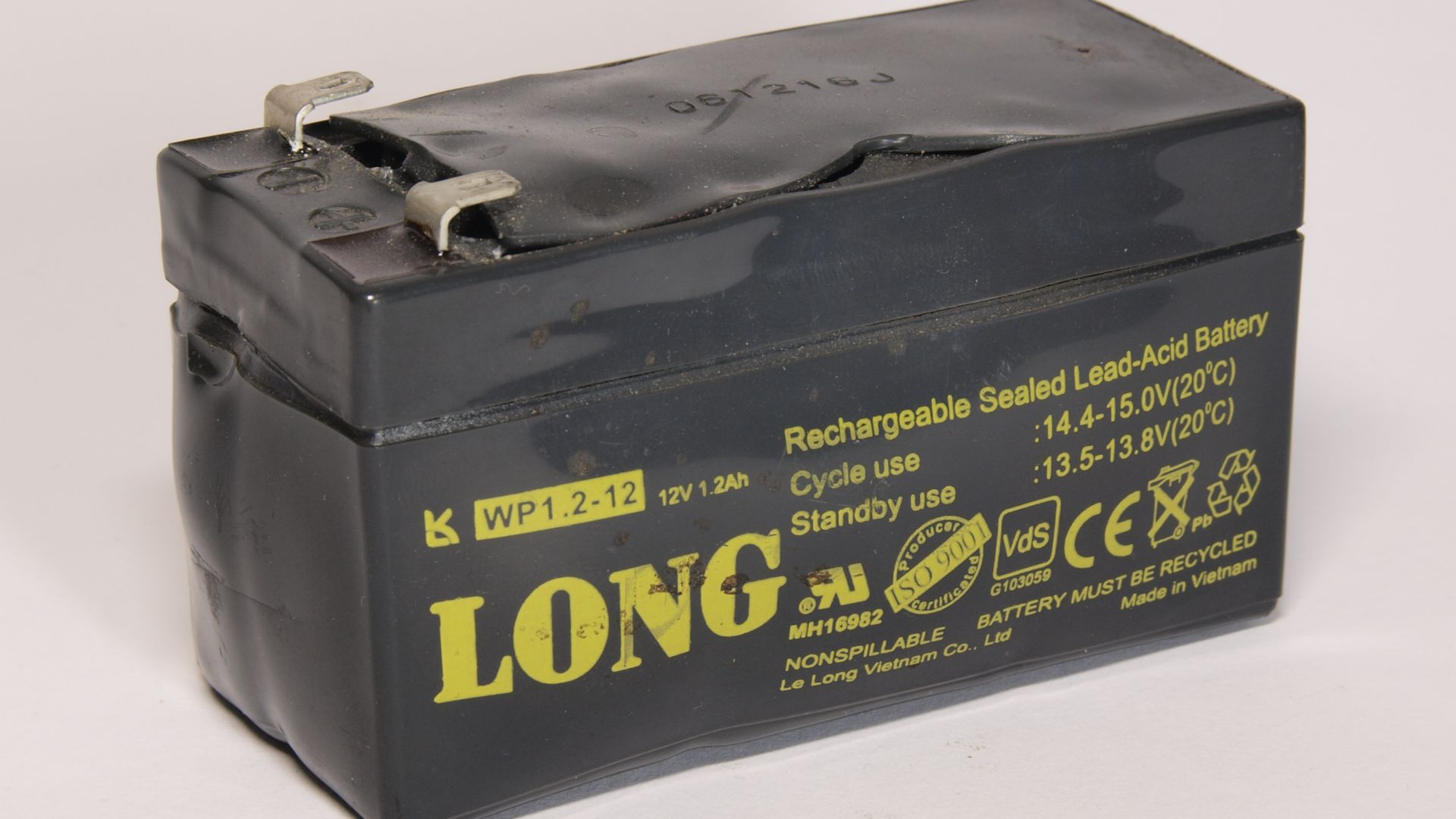 A used stand by AGM lead battery 12 Volts 1.2 Ah. Puffed up caused by an internal defect or inproper charging conditions. Model LONG WP1.2-12. Made in Vietnam. Made in the early 2010s.
