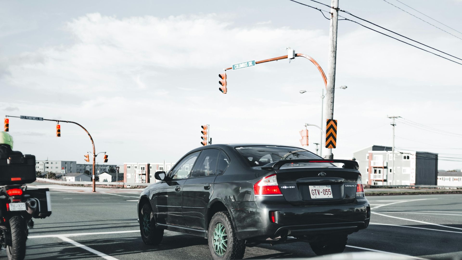 A motorcycle and car wait at a busy city intersection under traffic lights.