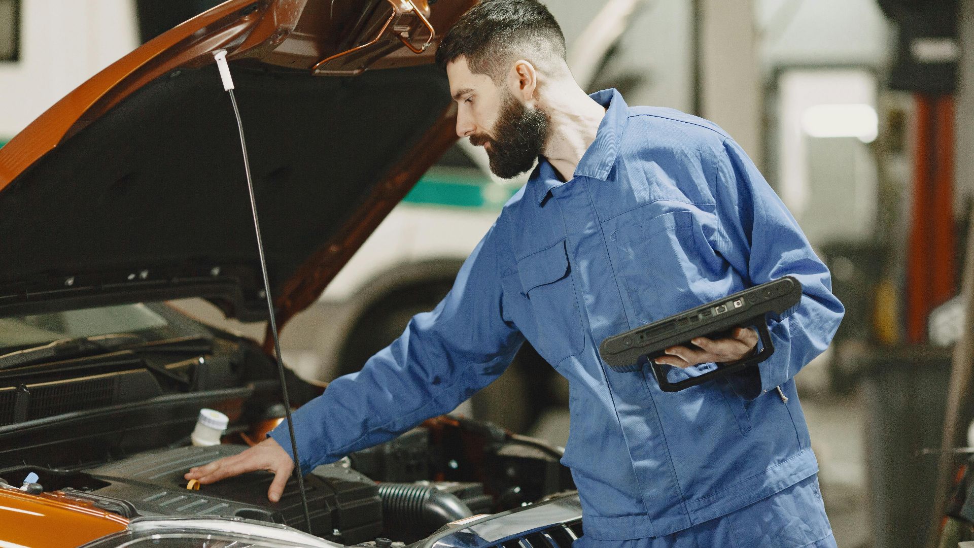 Professional mechanic examining a car engine under an open hood in a garage setting.