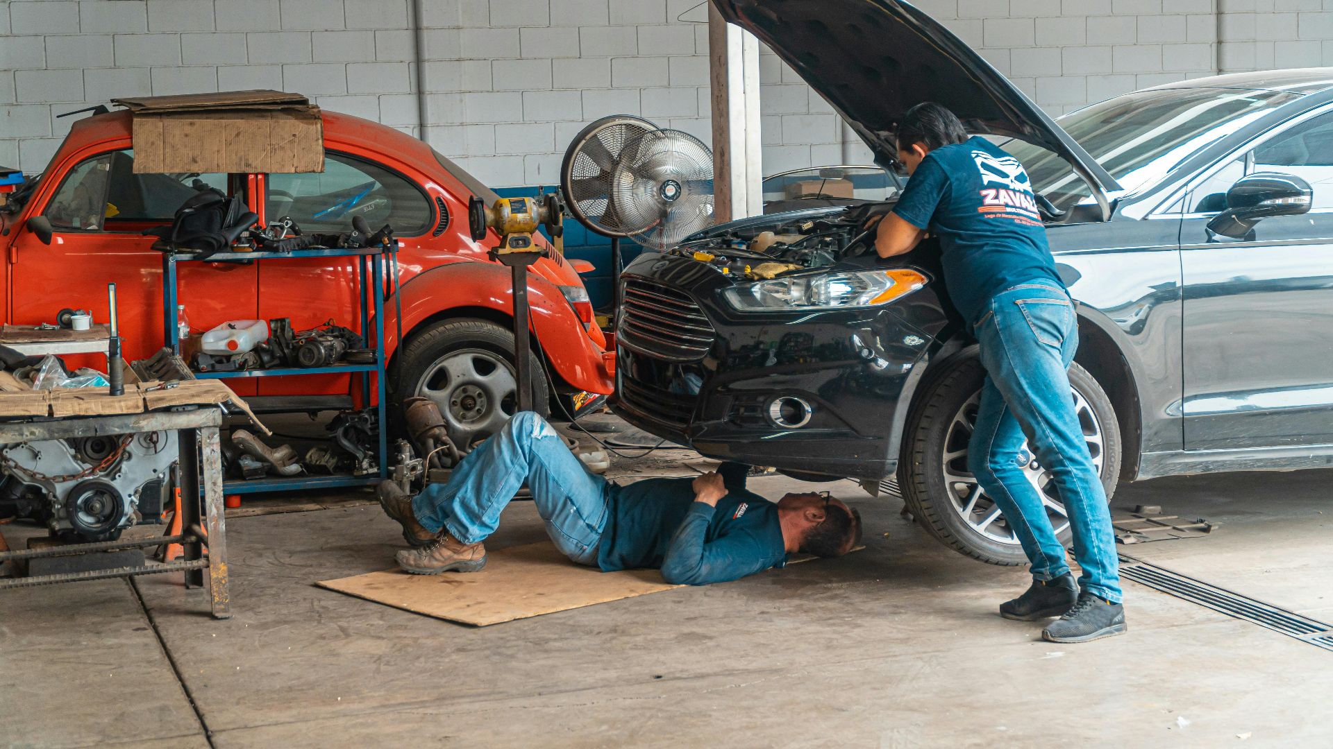 Mechanics working in an automotive workshop, repairing cars and performing maintenance.