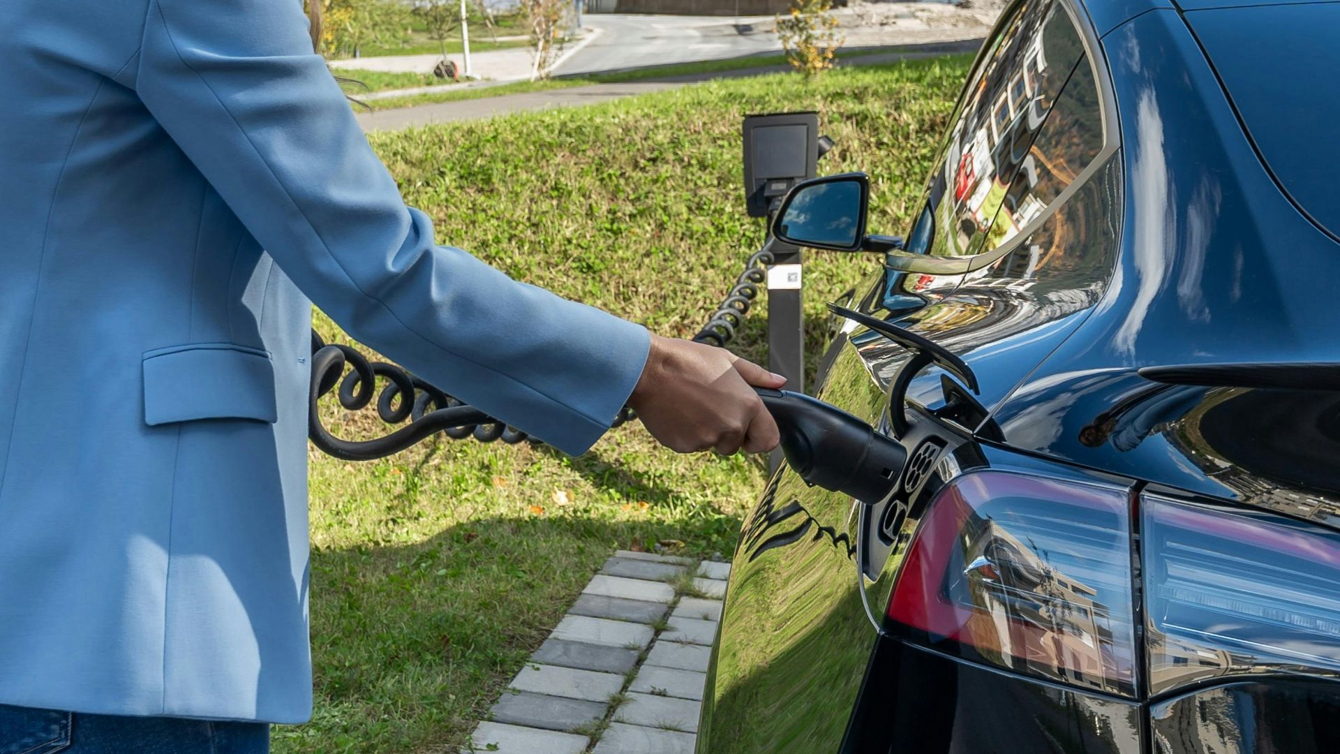Person connecting an electric car to a charging station outdoors, showcasing green energy transition.