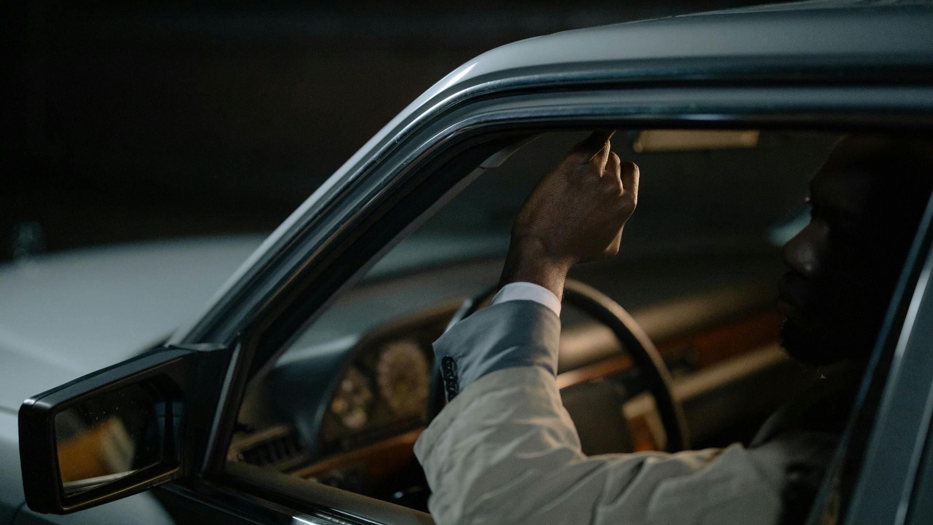Man inside a car adjusting the rearview mirror in dim lighting, conveying a nighttime drive ambiance.