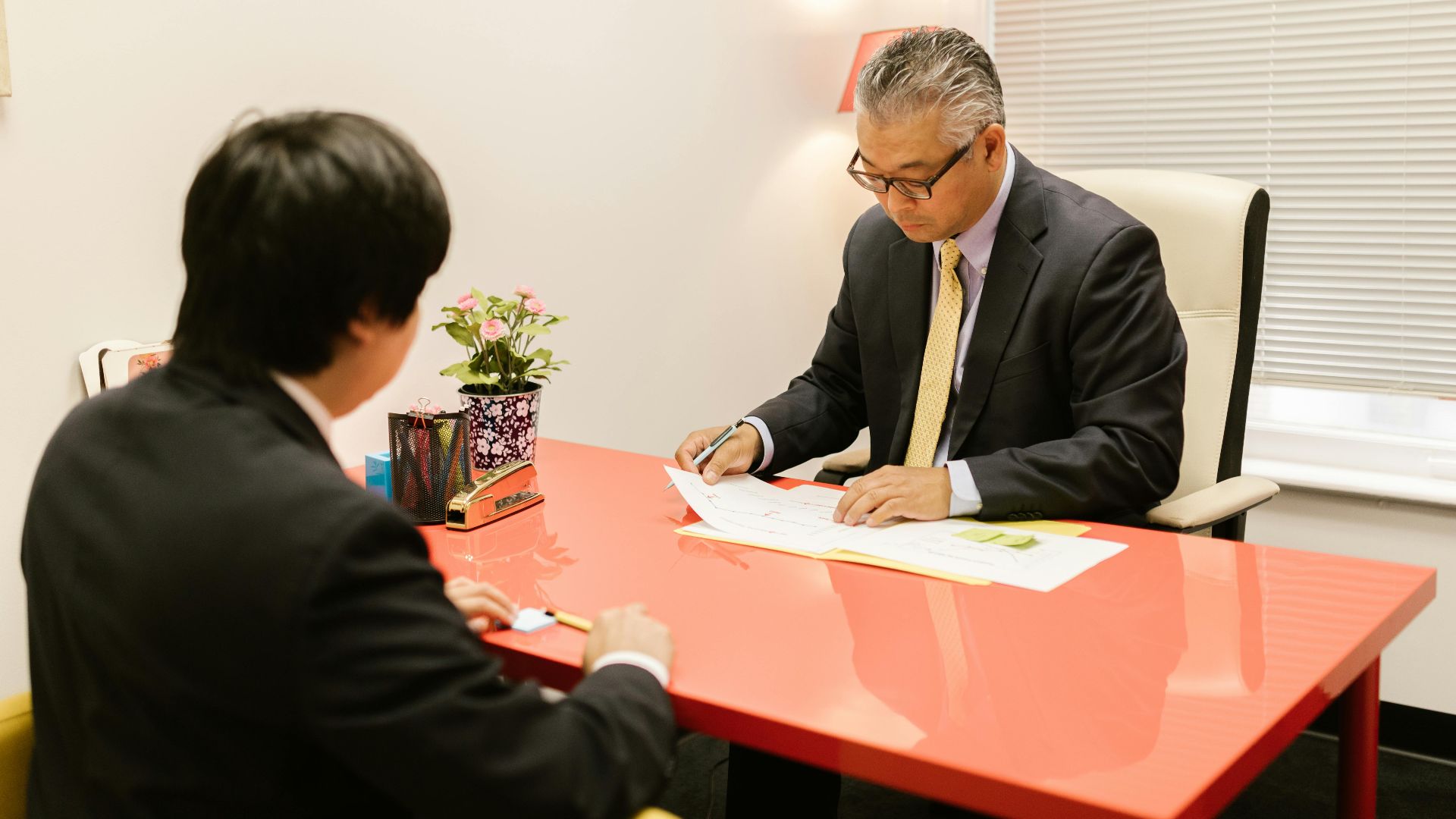 Two professionals discussing documents in a modern office with a red desk.