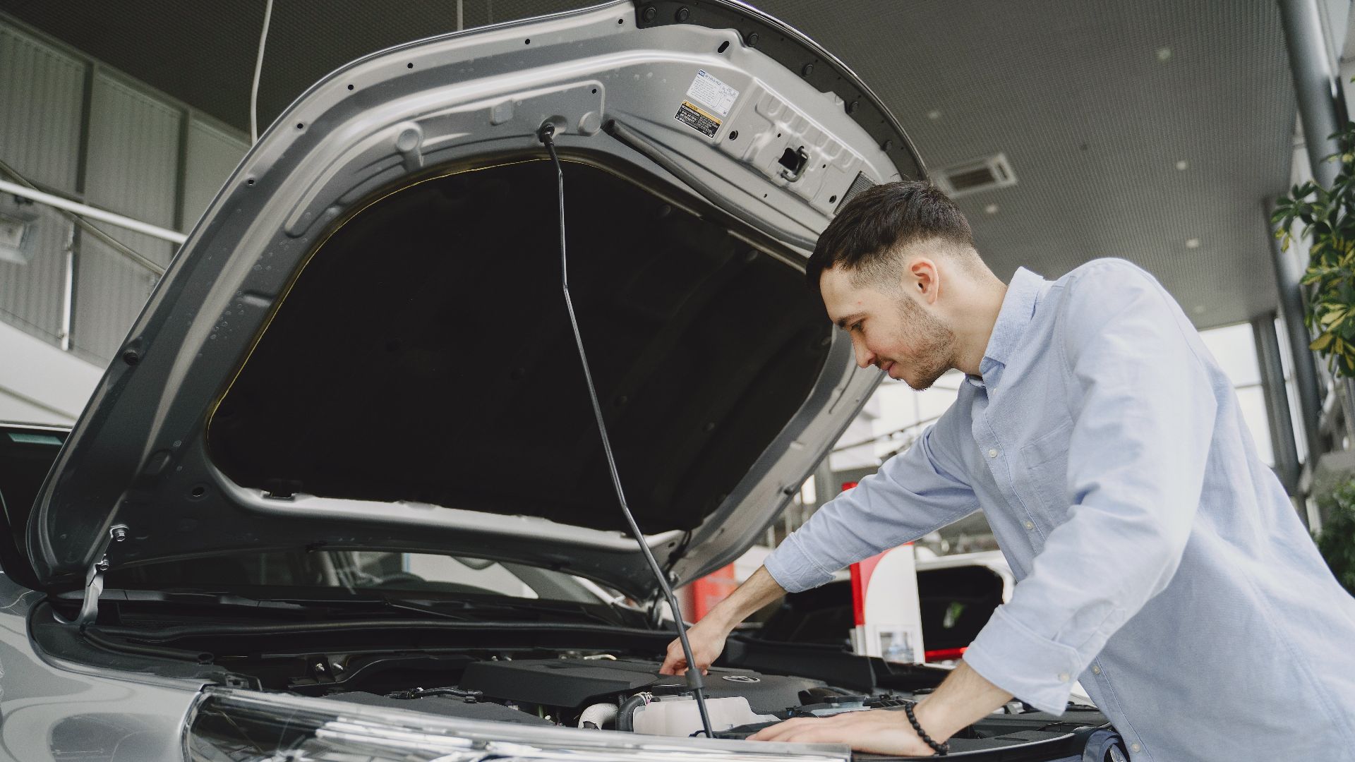 A man in a blue shirt examines a car's engine in a modern vehicle showroom.