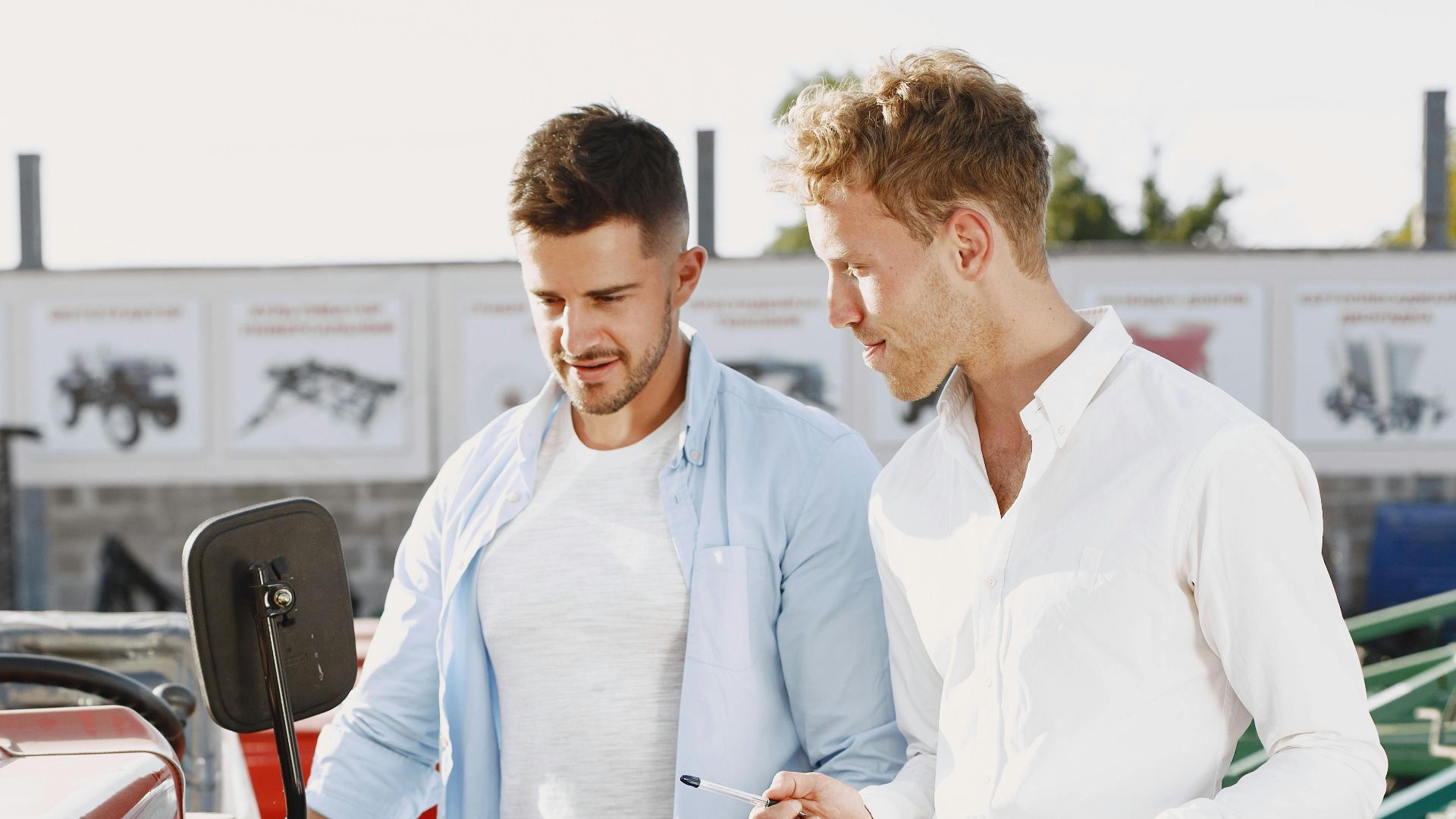 Two men having a discussion about a red tractor in an outdoor setting, possibly negotiating a deal.