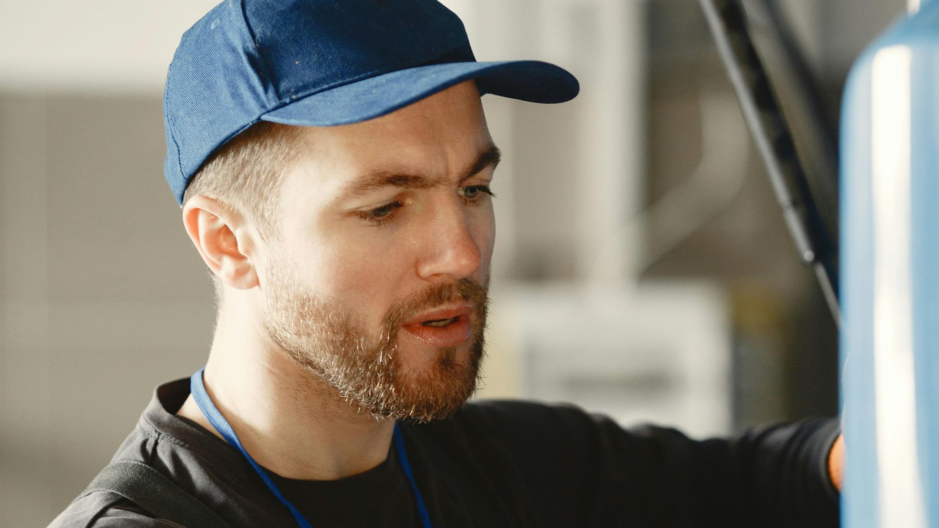 A male mechanic in a blue cap works on a vehicle indoors, focusing intently.