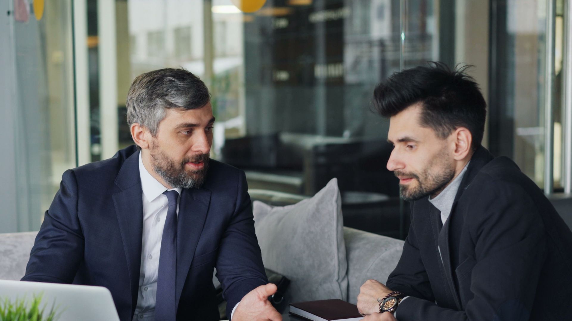 Two businessmen in a café having a professional discussion with coffee and a laptop.