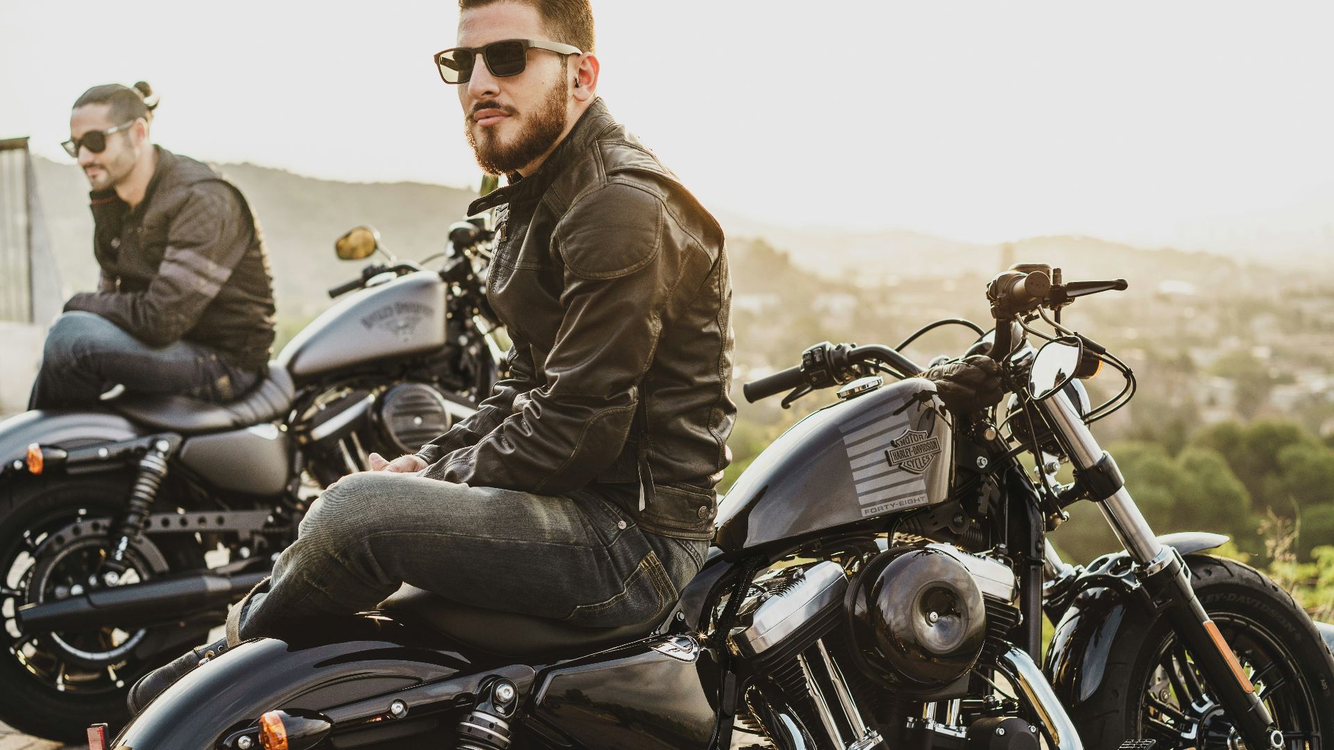 two men sitting on two parked cruiser motorcycles