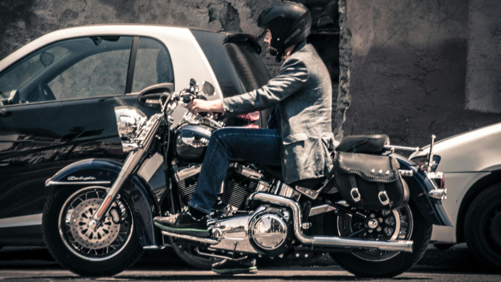 Man on a Harley Davidson Harley, wearing a helmet, rides through an urban street alongside cars.