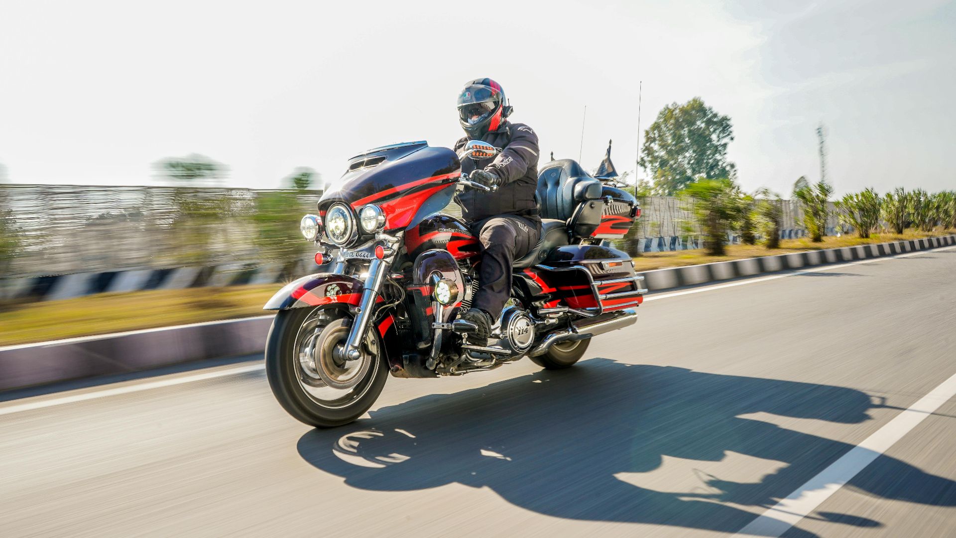 Man on a Harley-Davidson motorcycle riding on an open highway in daylight.