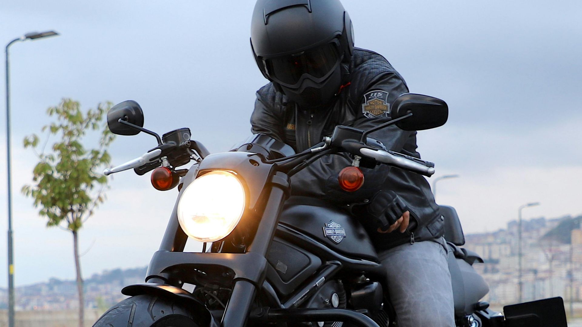 A biker in black leather gear rides a sleek cruiser motorcycle on an urban road.