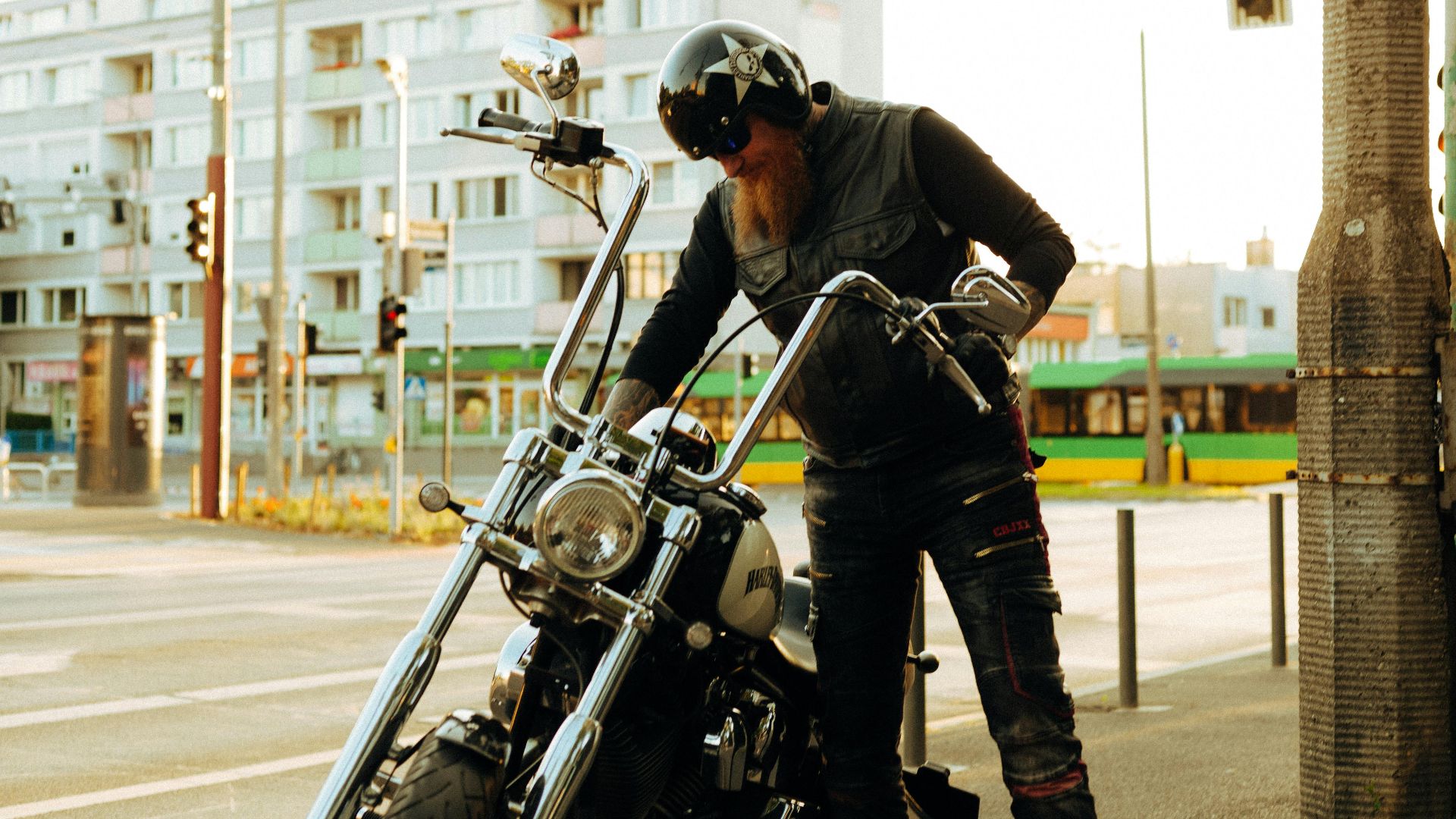 A bearded biker standing with a Harley-Davidson on a city street in Poznań, Poland.