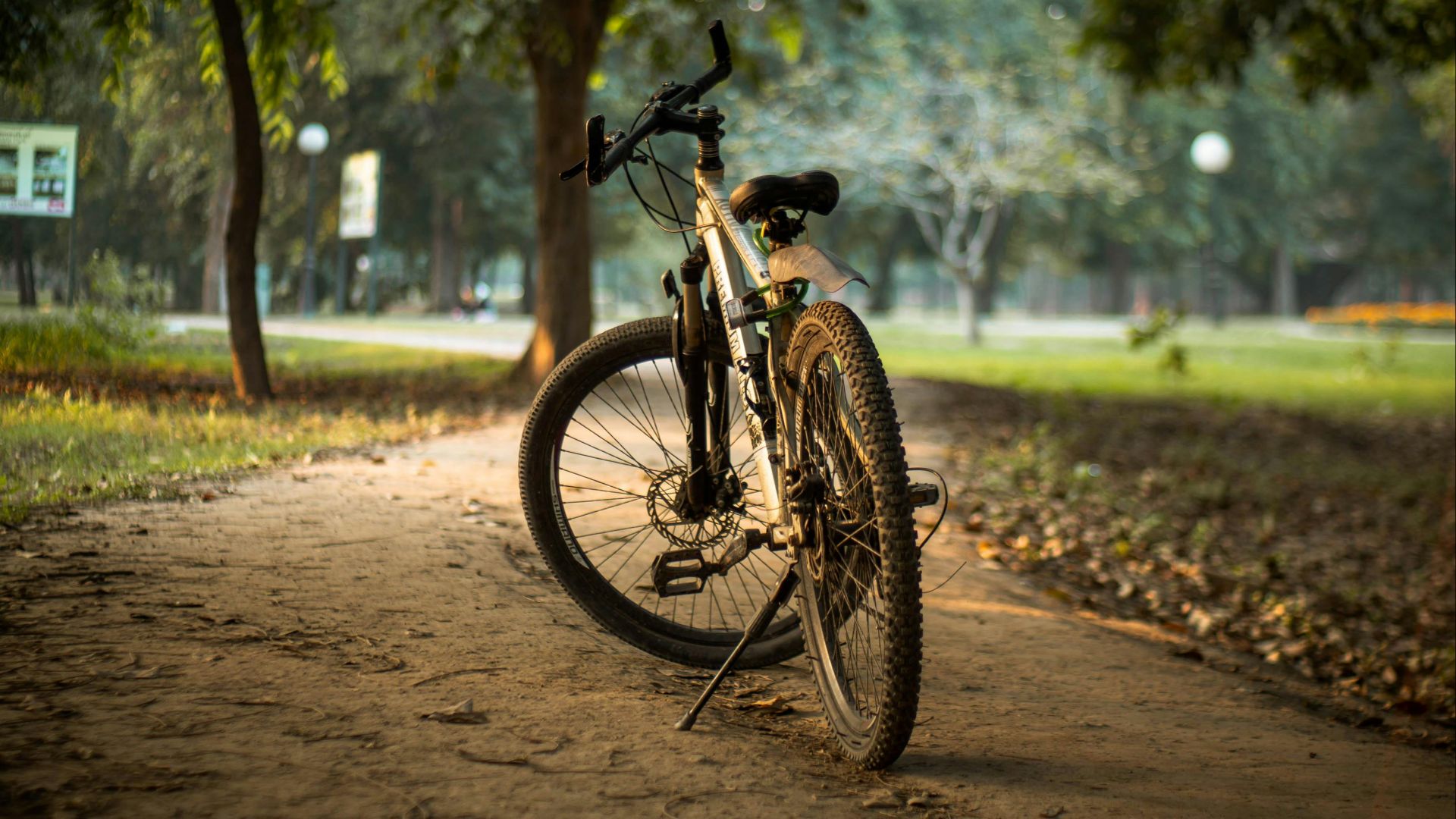 A mountain bike is parked on a dirt path in a lush park setting, surrounded by trees.