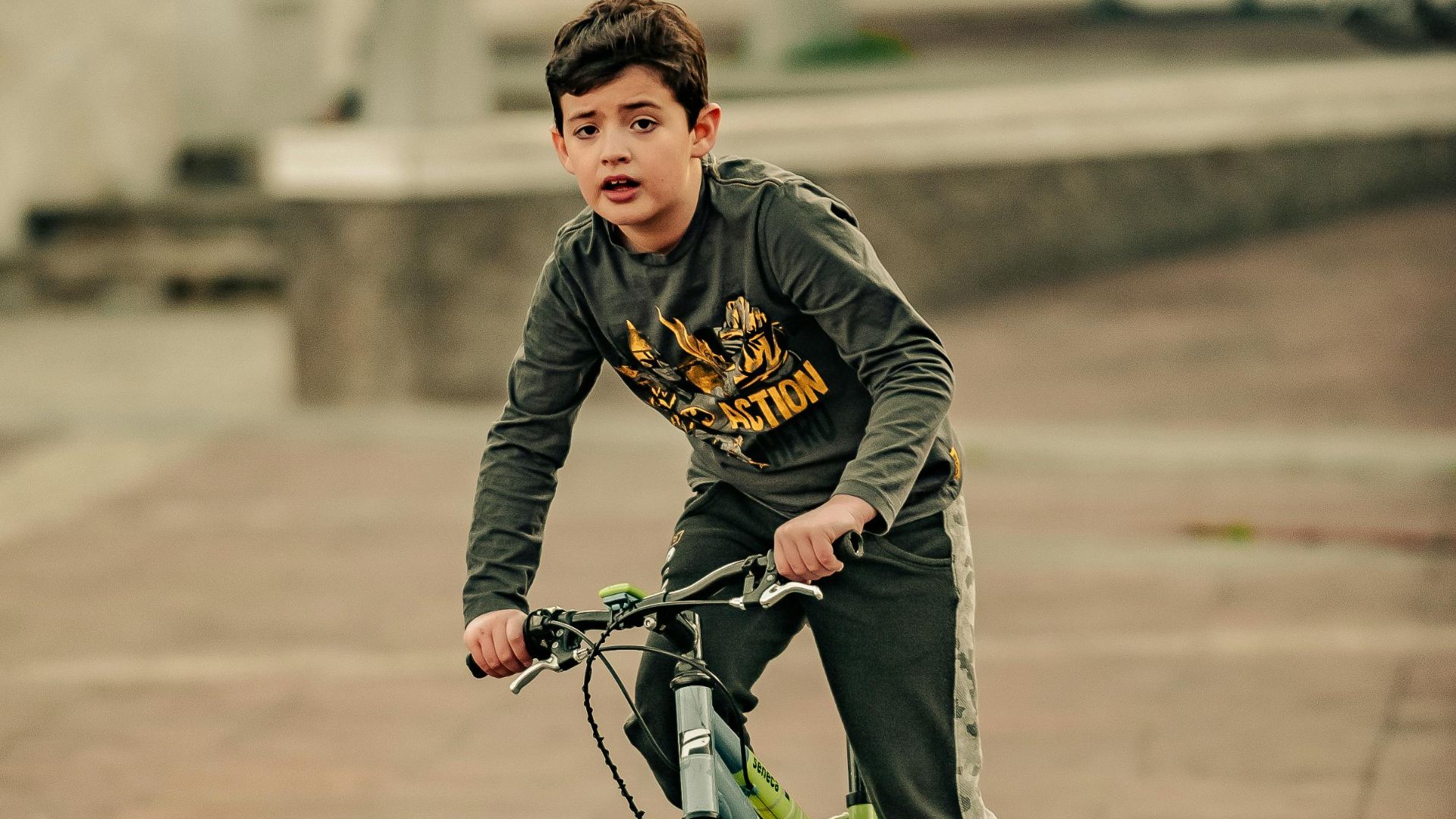 Ethnic child in casual wear driving bike on tiled pavement behind staircase in town while looking at camera in daytime