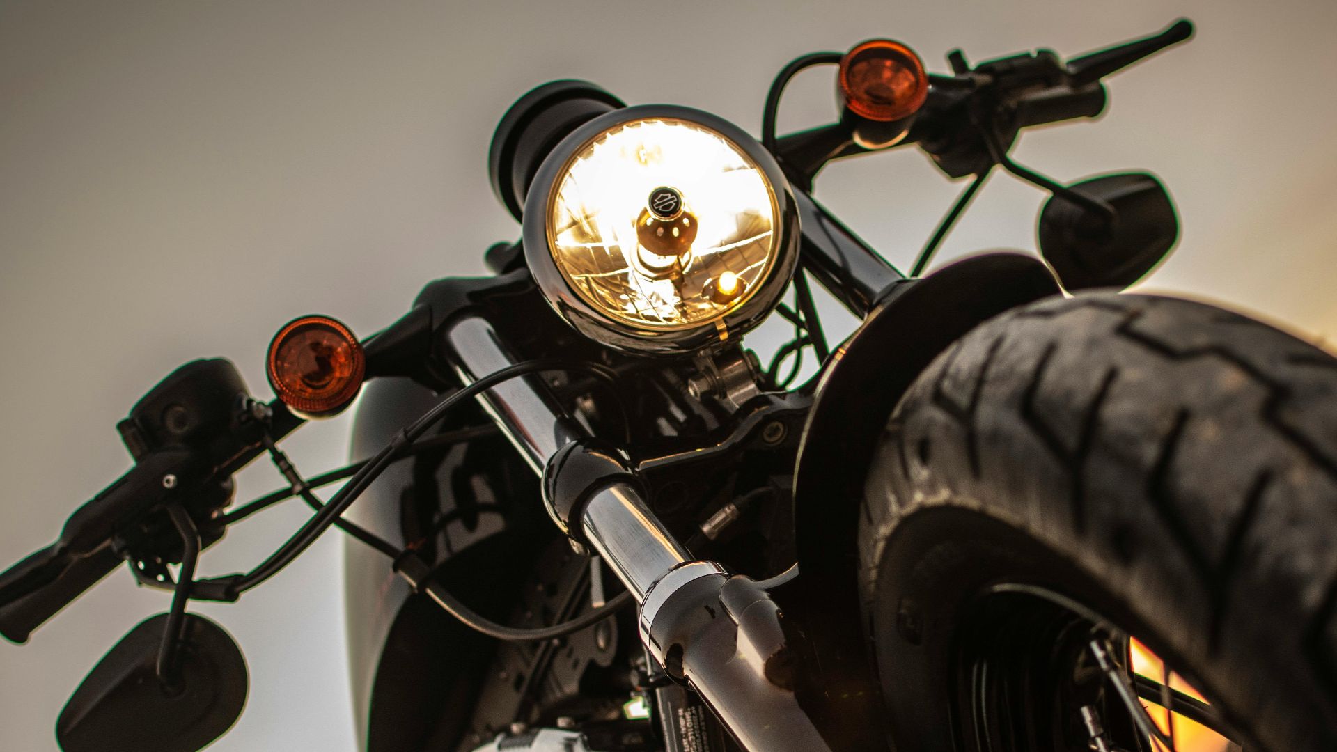 Dramatic close-up of a classic motorcycle's headlight with a low angle view at sunset.