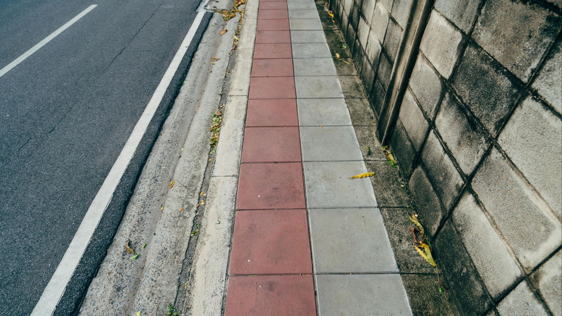 View of a colorful urban sidewalk with a textured wall beside it.