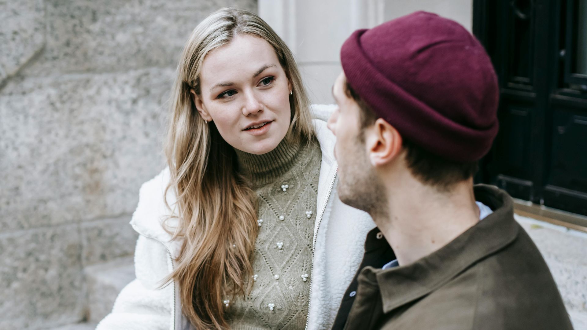 Man and woman talking sitting on steps outside house and having hot beverage in paper cups