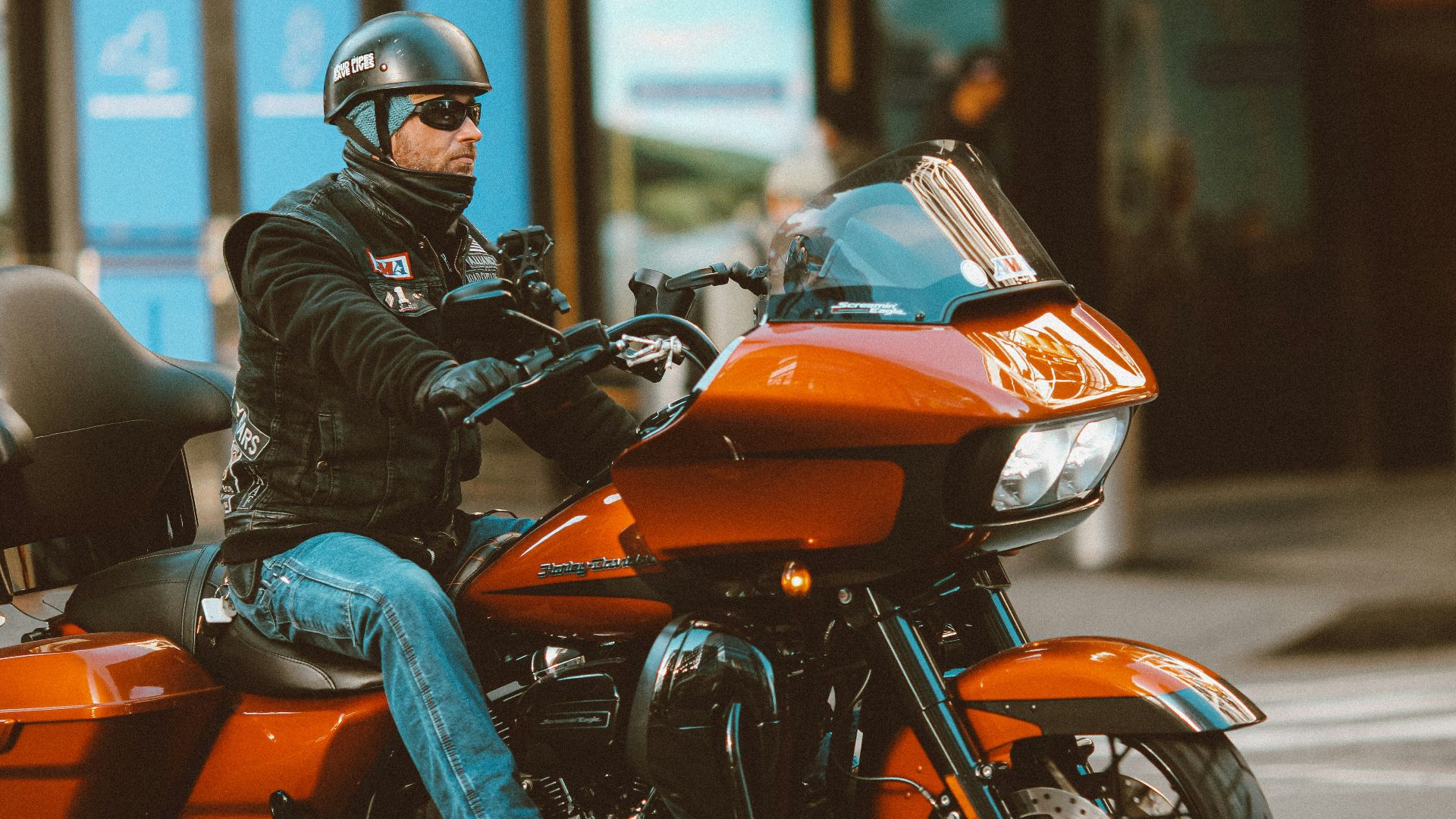 man in black leather jacket and blue denim jeans riding orange and black motorcycle